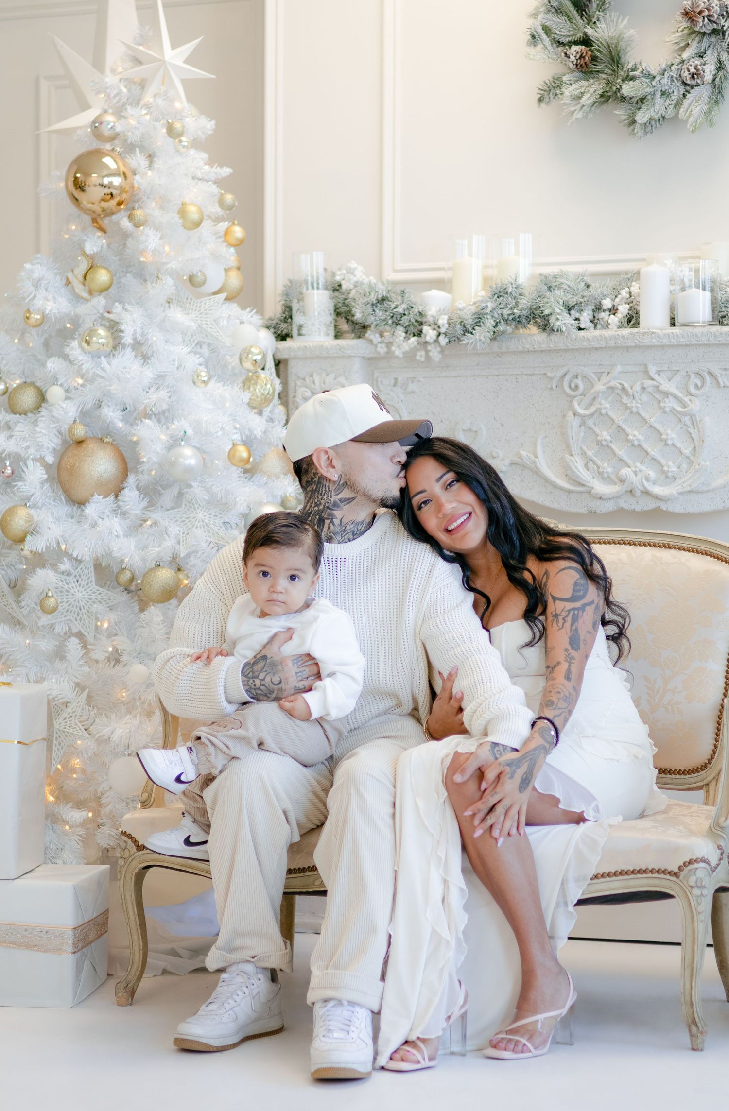 Candid family moment captured on elegant white couch with festive white Christmas tree in background.
