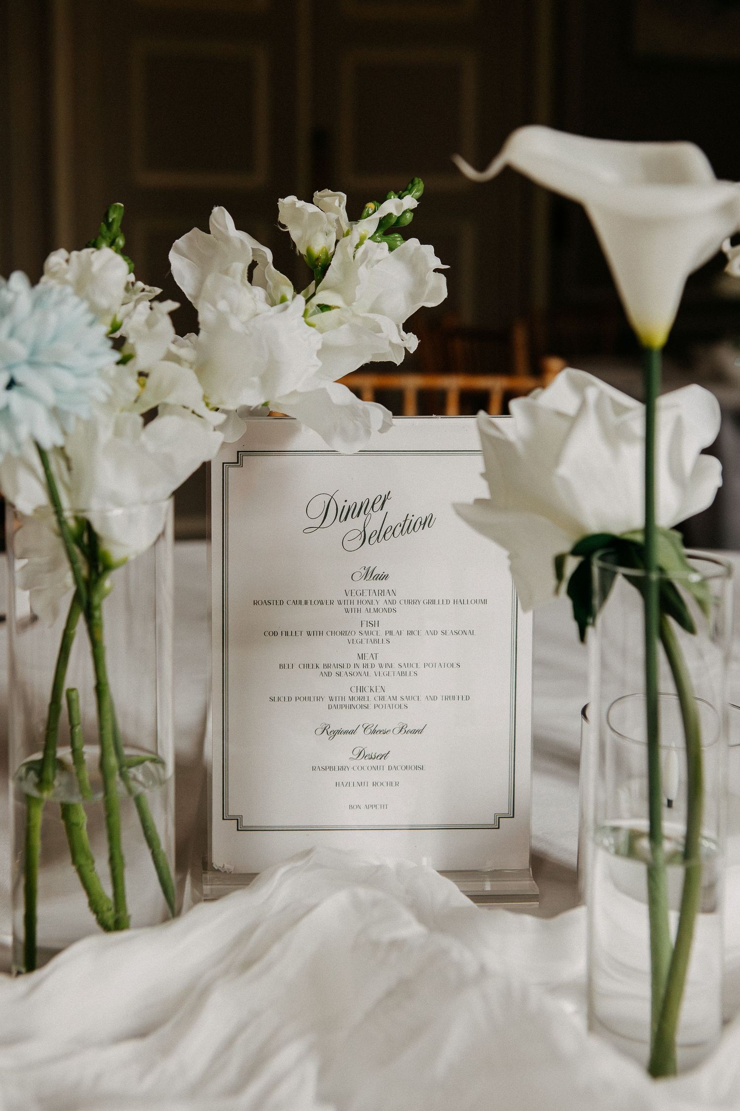 Elegant wedding table with white floral arrangements and a framed dinner selection menu card.