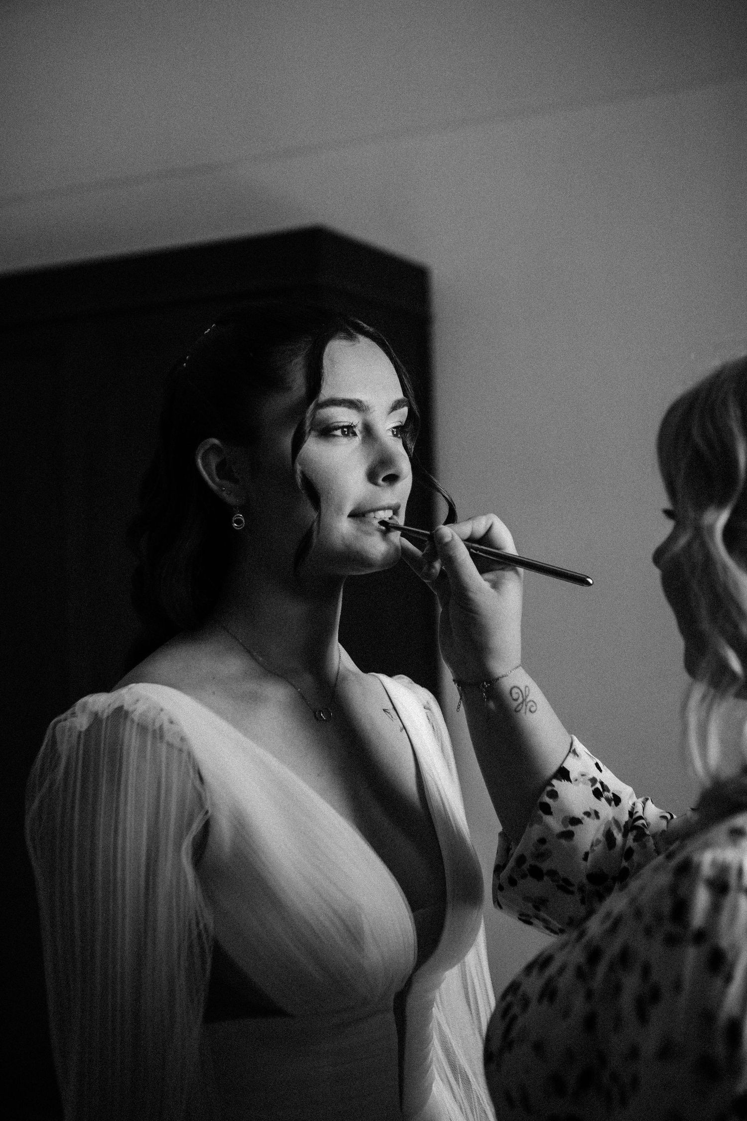 Black and white photo of a makeup artist applying lipstick to a bride in a white wedding dress.