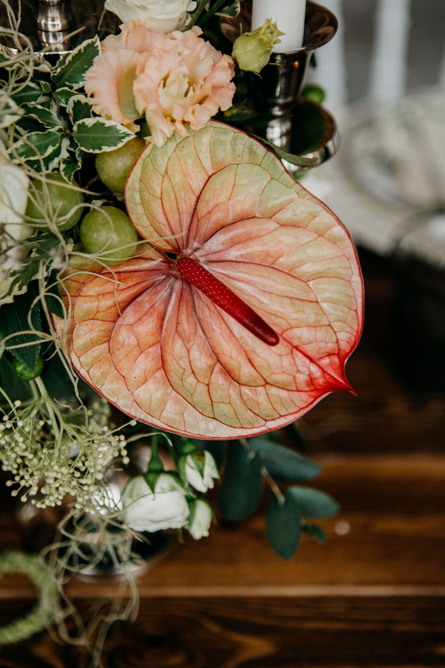 Close-up of a pink anthurium flower surrounded by white roses and green foliage in a wedding arrangement.