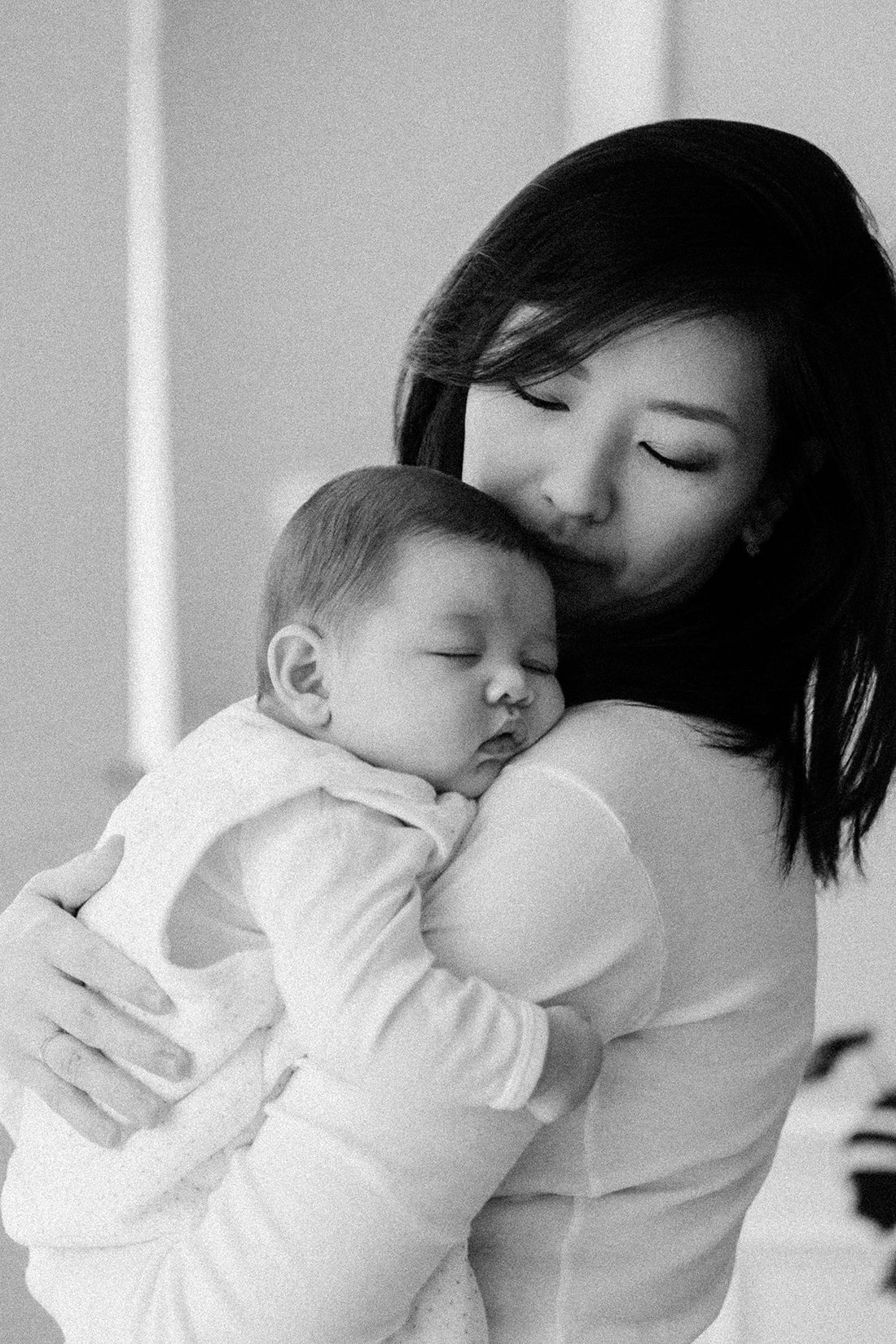 Black and white photo of mother kissing sleeping newborn baby tenderly.