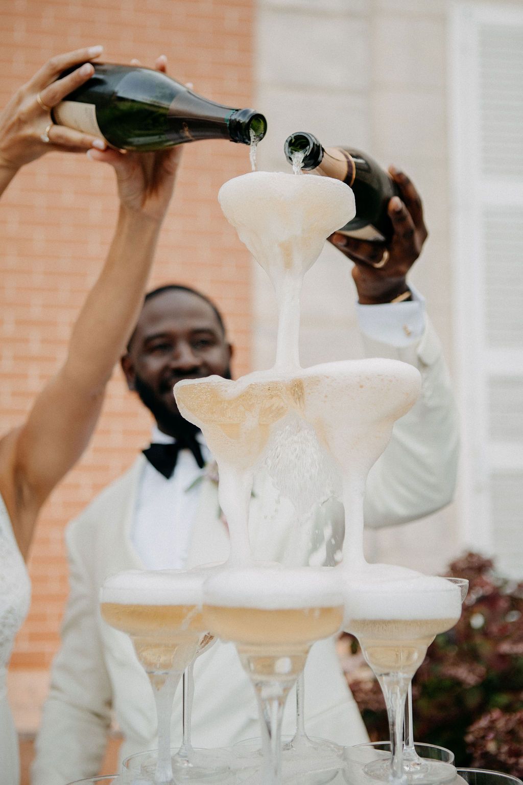 Close-up of champagne overflowing a tiered crystal glass tower as bride and groom pour bottles together.