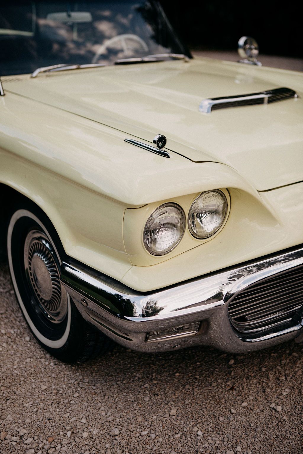 Detail shot of a vintage cream Ford Thunderbird classic car with dual headlights and chrome bumper.