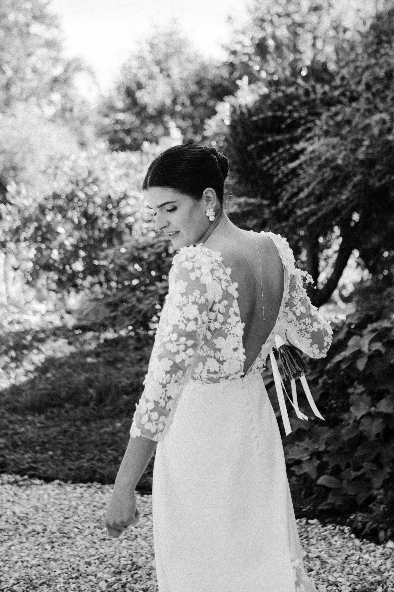 Black and white portrait of bride in floral lace open-back wedding dress with elegant updo in garden setting.