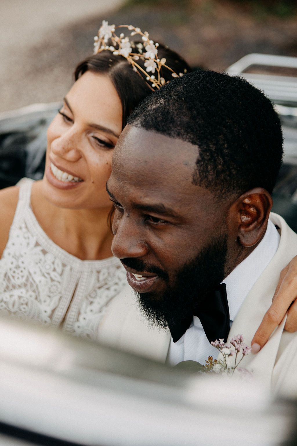 Close-up of smiling interracial bride and groom in a vintage convertible car on their wedding day.