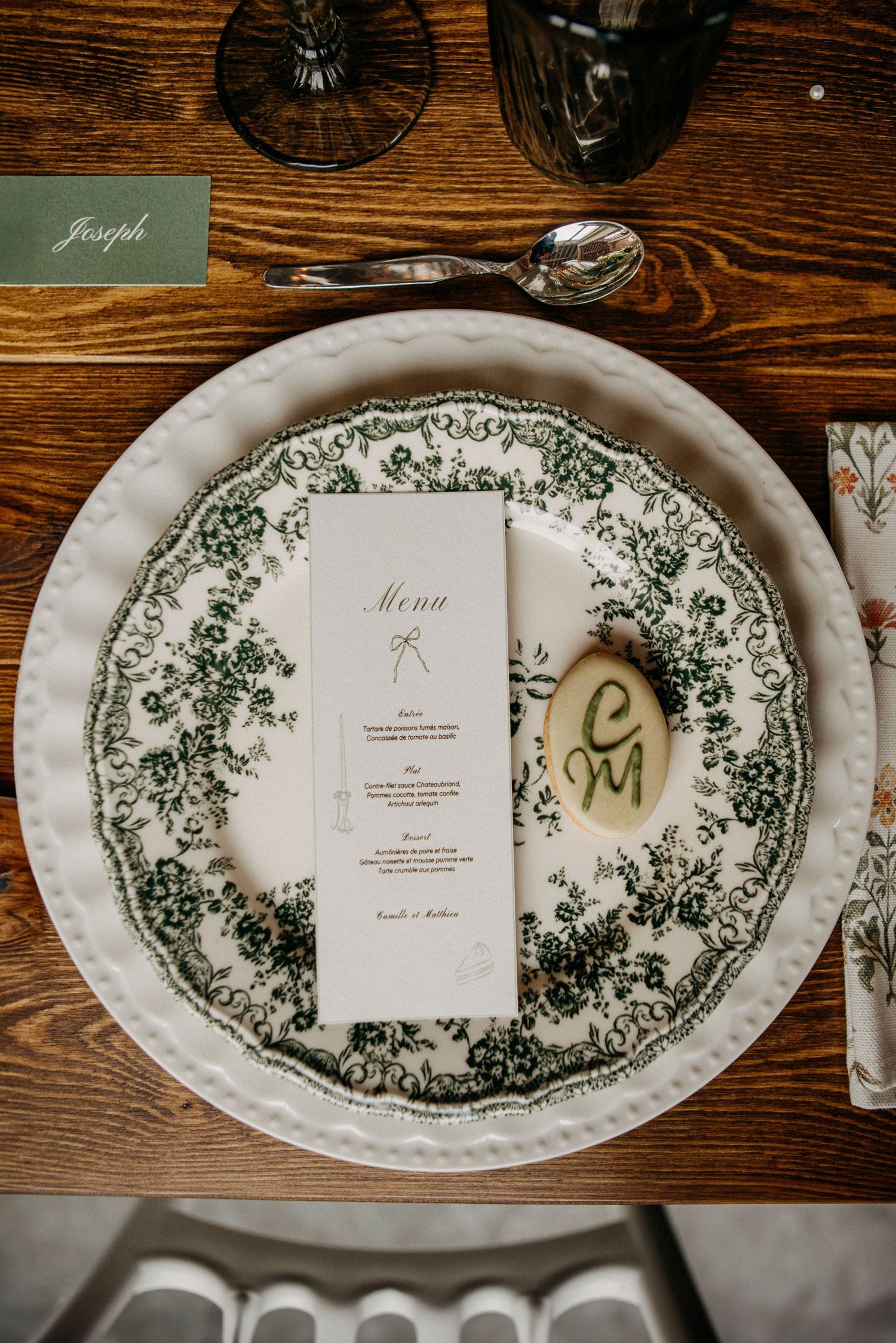Wedding place setting with green floral plate, menu card, and personalized stone detail.