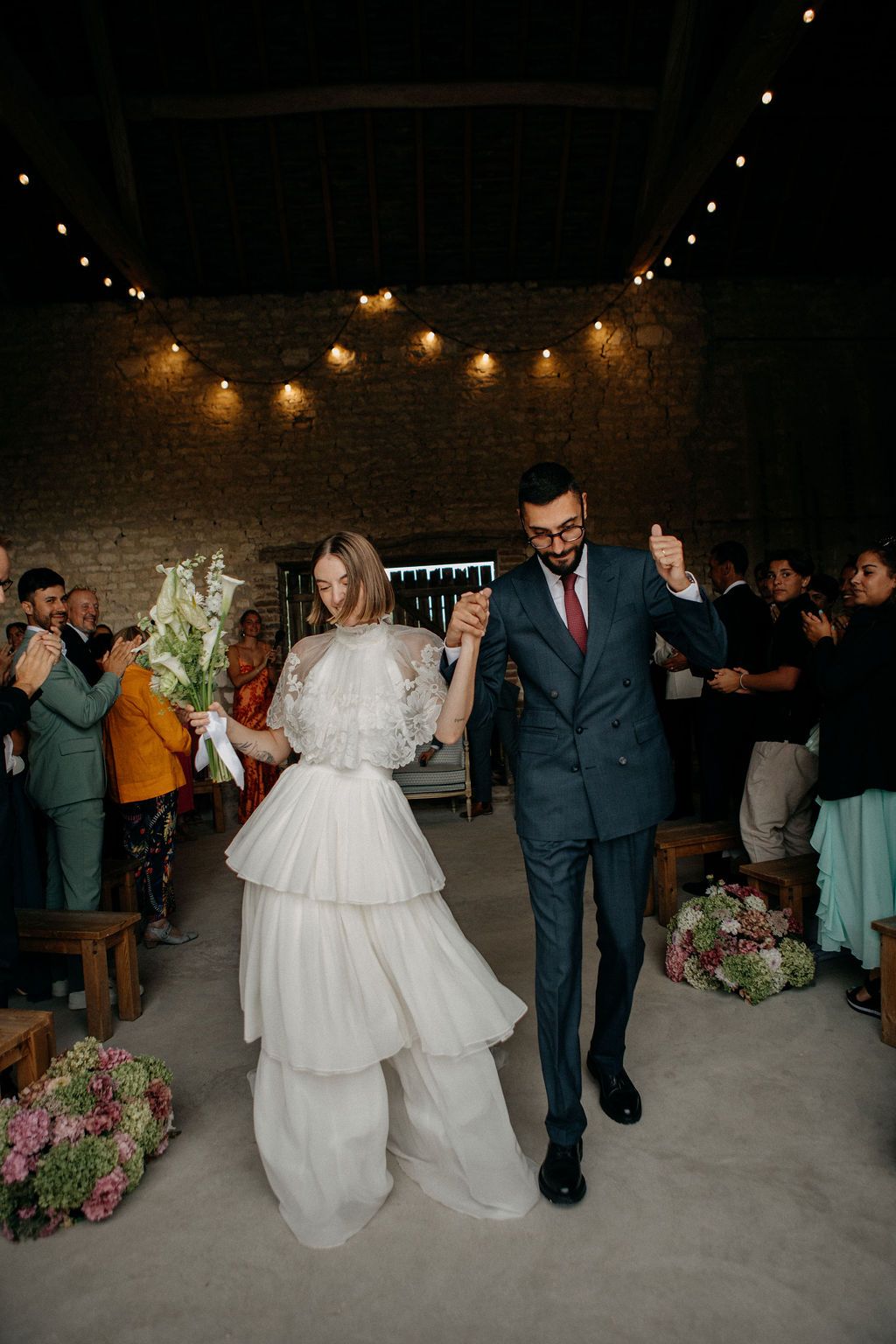 Joyful newlyweds walk down the aisle hand in hand after rustic barn wedding ceremony.