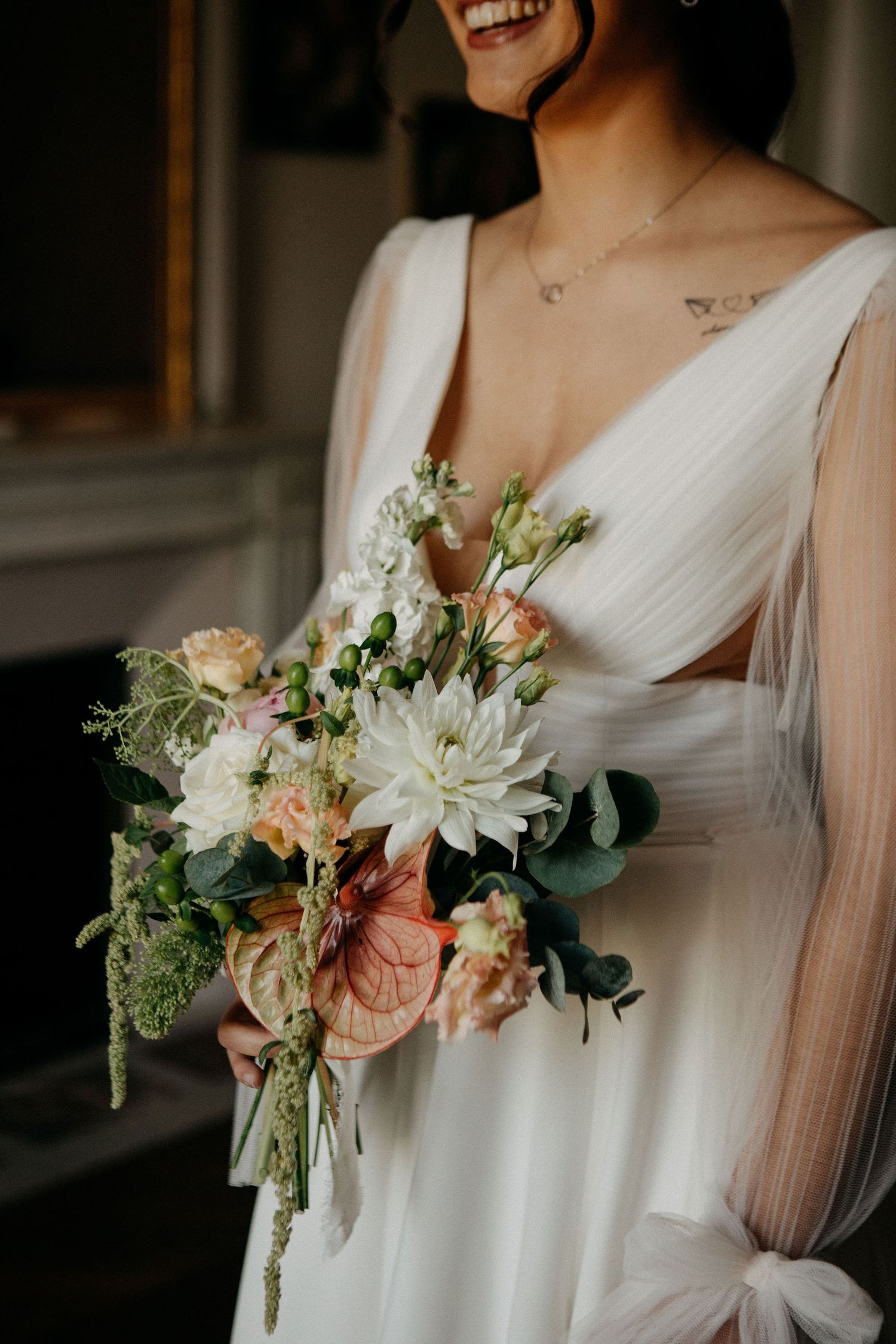 Laughing bride in a white V-neck wedding dress holding a lush bouquet with dahlias and anthurium.