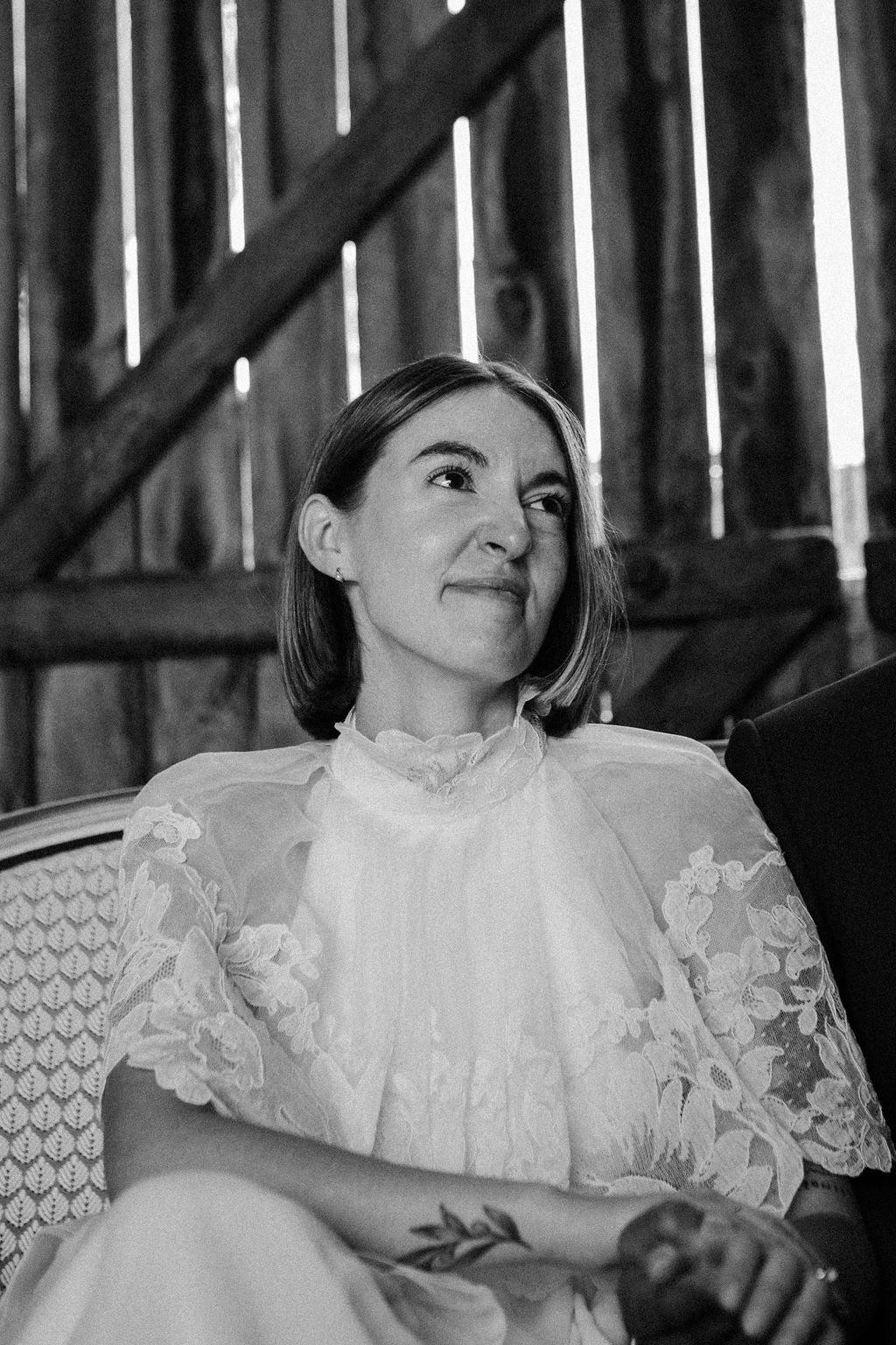 Black and white portrait of a bride in lace dress smiling in a rustic barn setting.