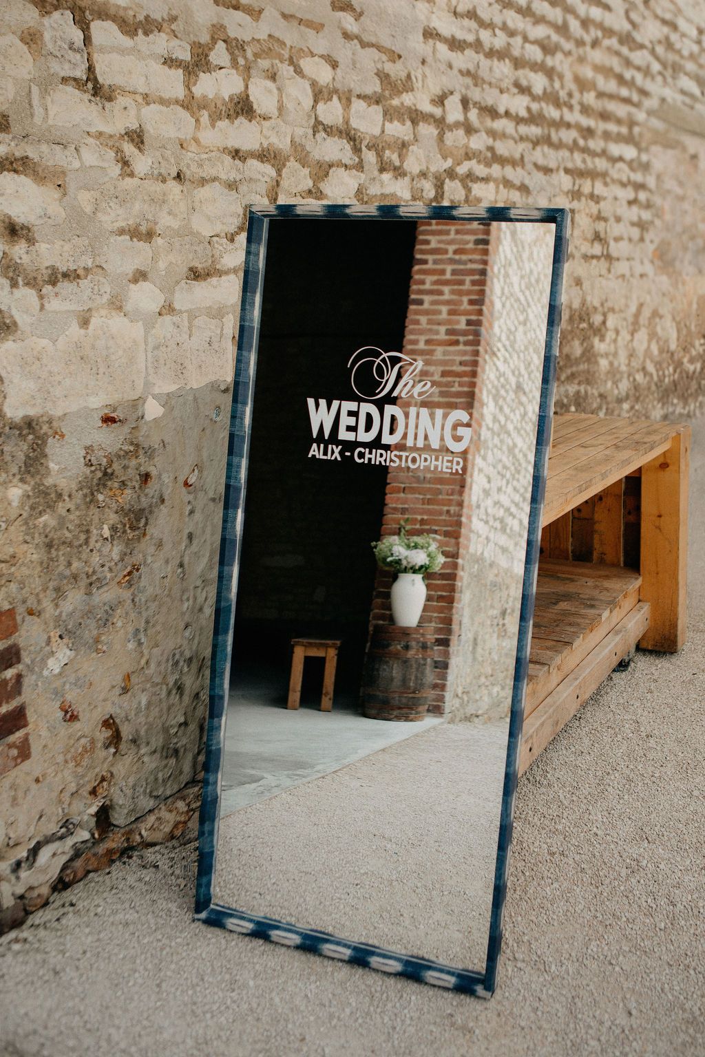 Wedding welcome mirror sign for Alix and Christopher leaning against rustic brick wall outdoors.