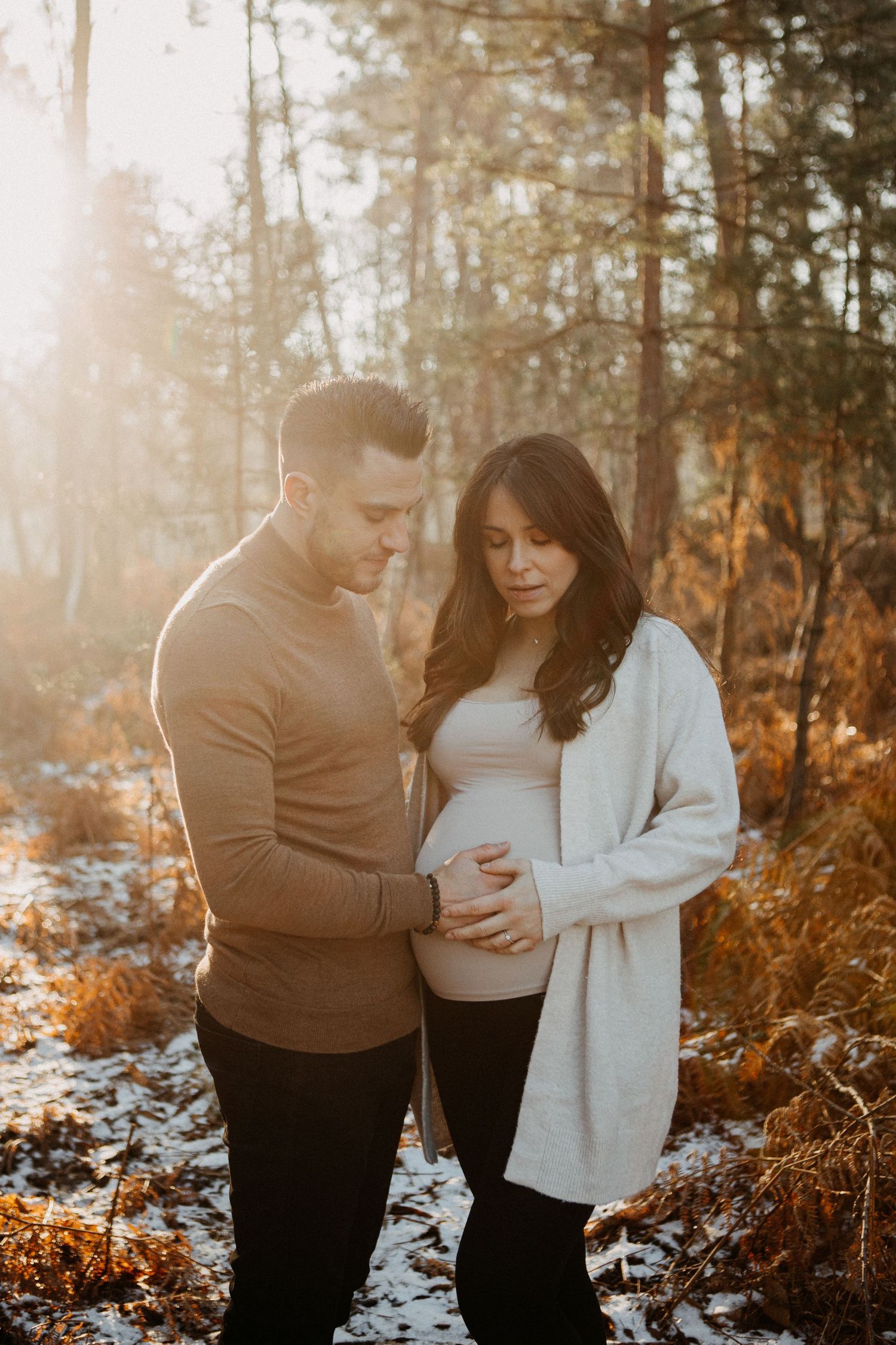 Man tenderly holding pregnant woman's belly in golden forest light during maternity shoot.