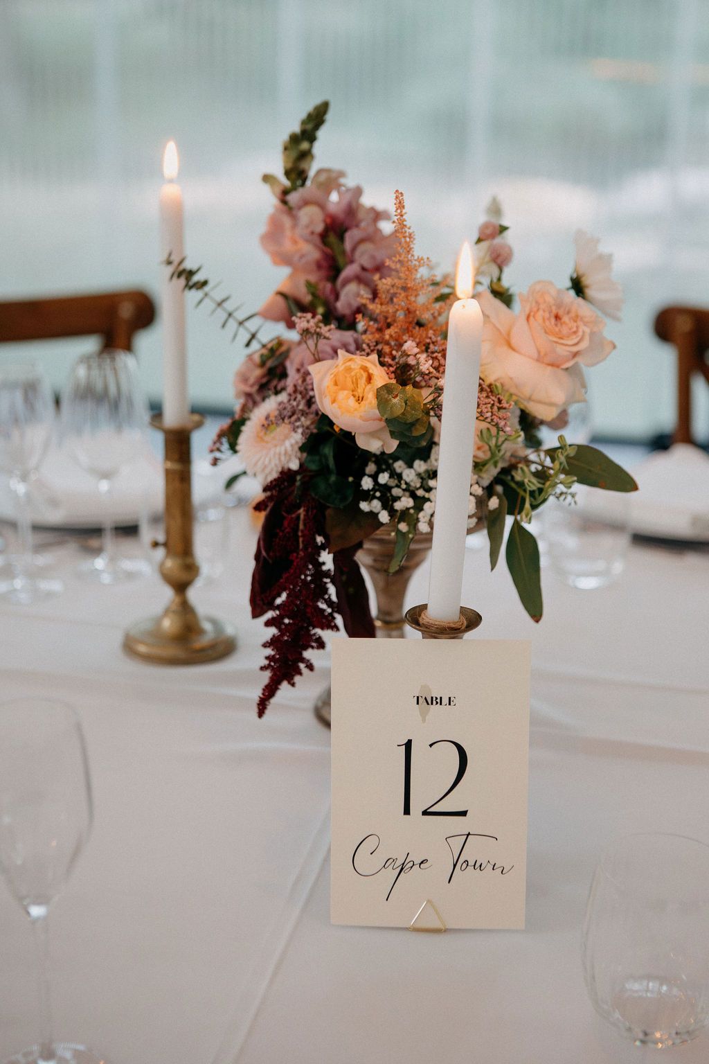 Elegant wedding table setting with a floral centerpiece, white taper candle, and table number 12 Cape Town sign.