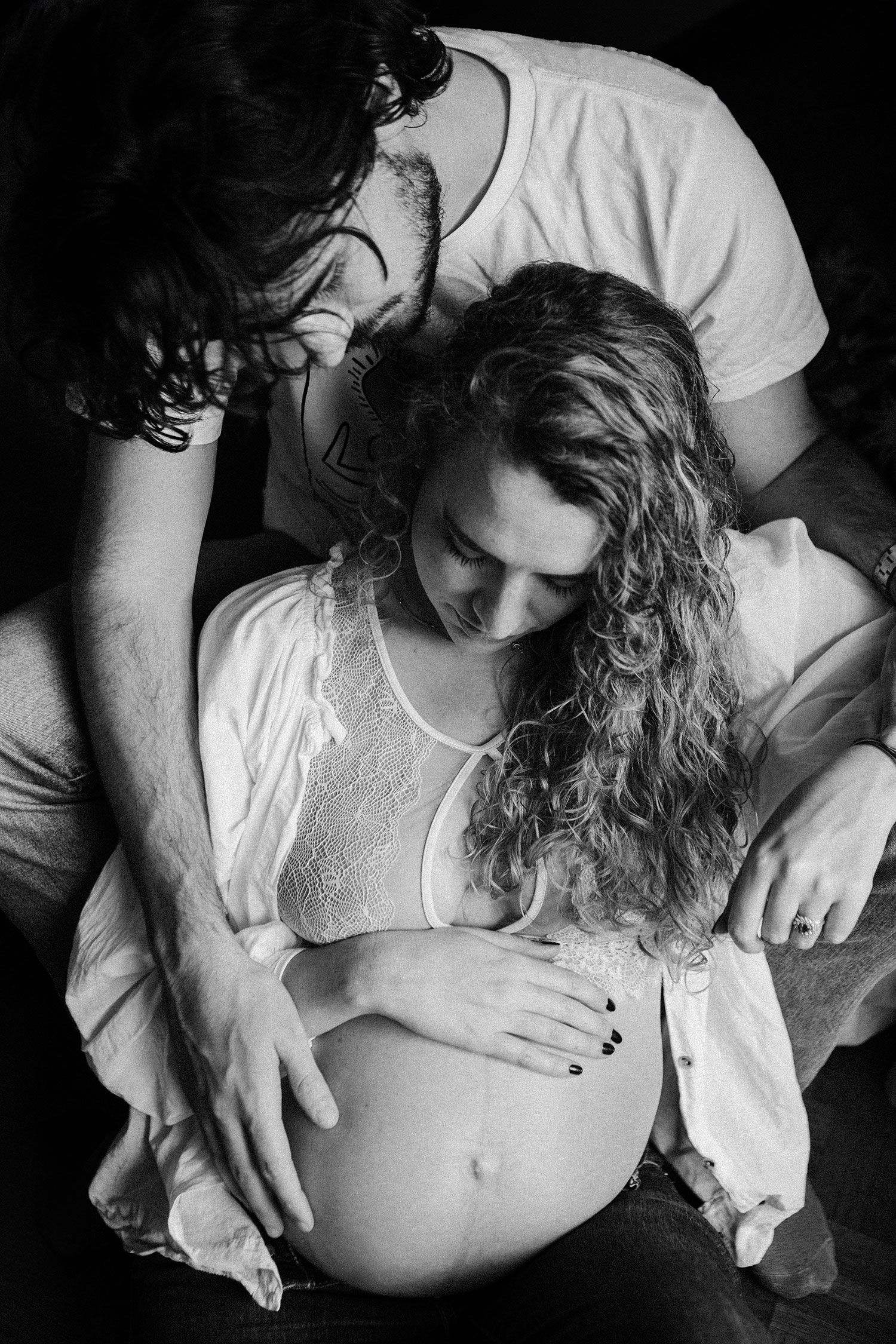 Black and white overhead photo of a couple tenderly cradling a pregnant belly together.