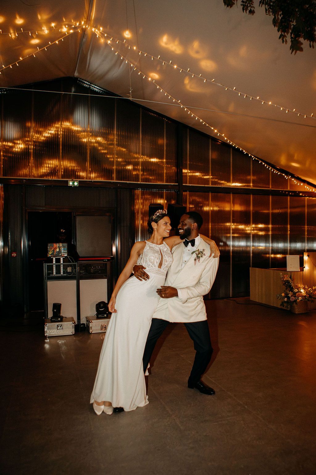 Bride and groom sharing their first dance under fairy lights in a warmly lit wedding venue.