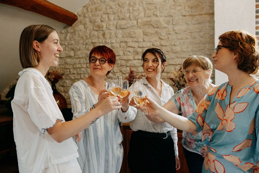 Five women in robes toasting with champagne glasses during bridal getting ready celebration.