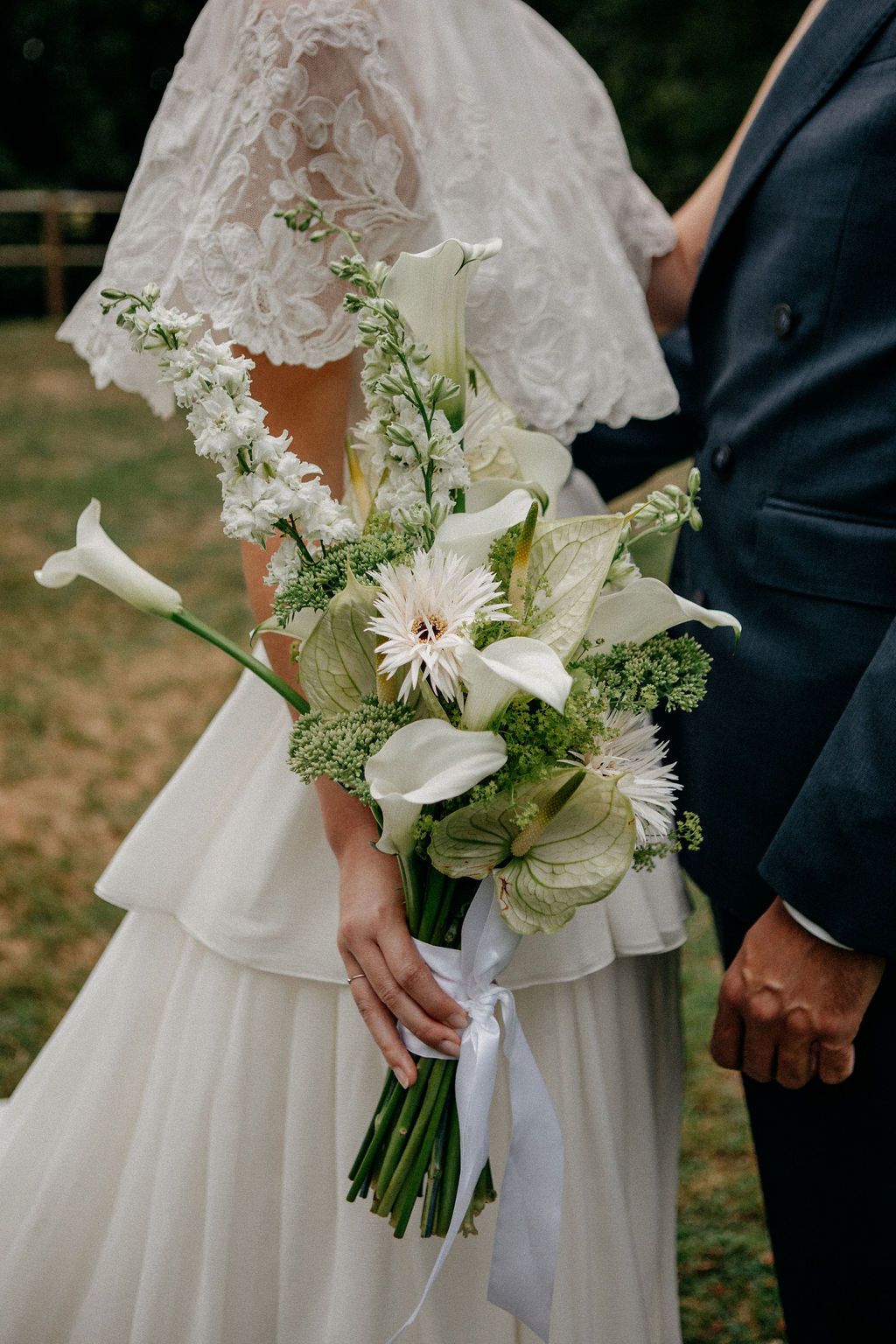 Close-up of a bridal bouquet featuring white calla lilies, anthurium, and green blooms tied with ribbon.