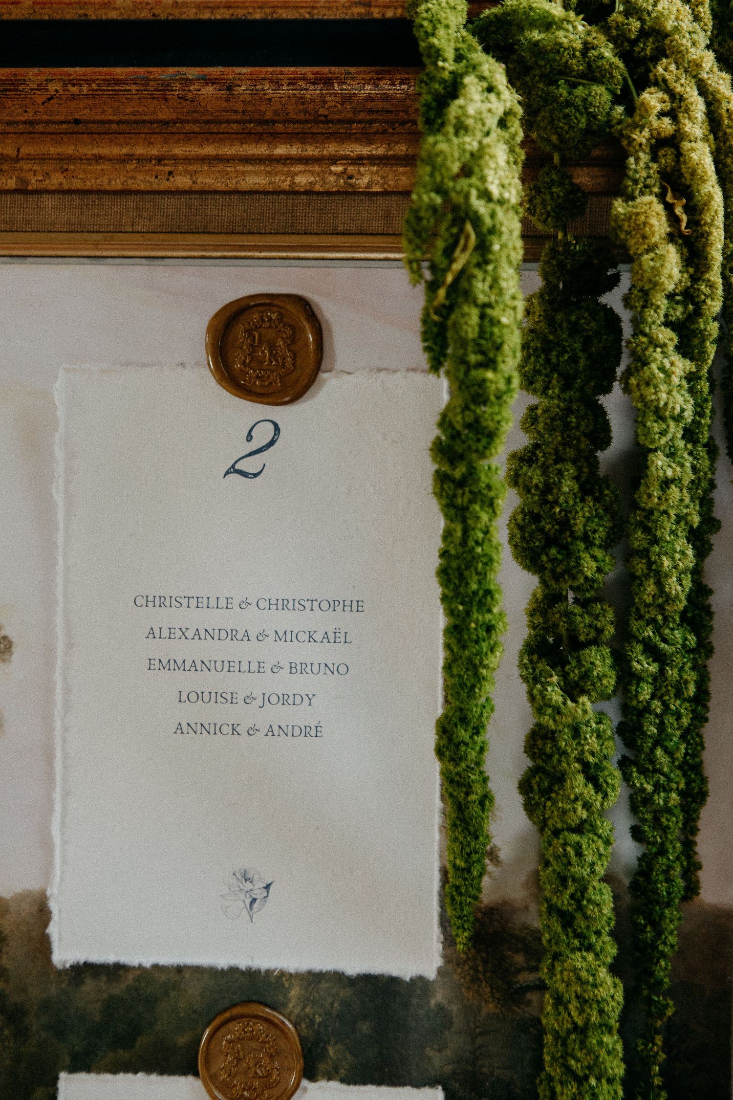 Elegant wedding seating chart with wax seal, handwritten names, and lush green amaranthus floral arrangement.
