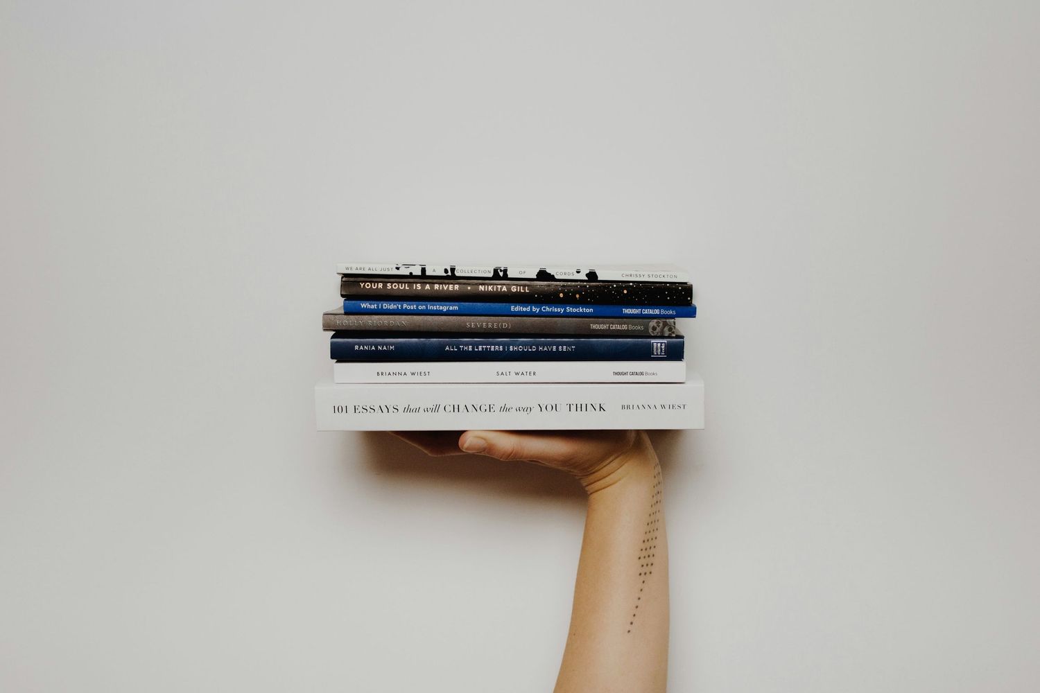 A hand holding a neatly stacked pile of books against a clean white background.