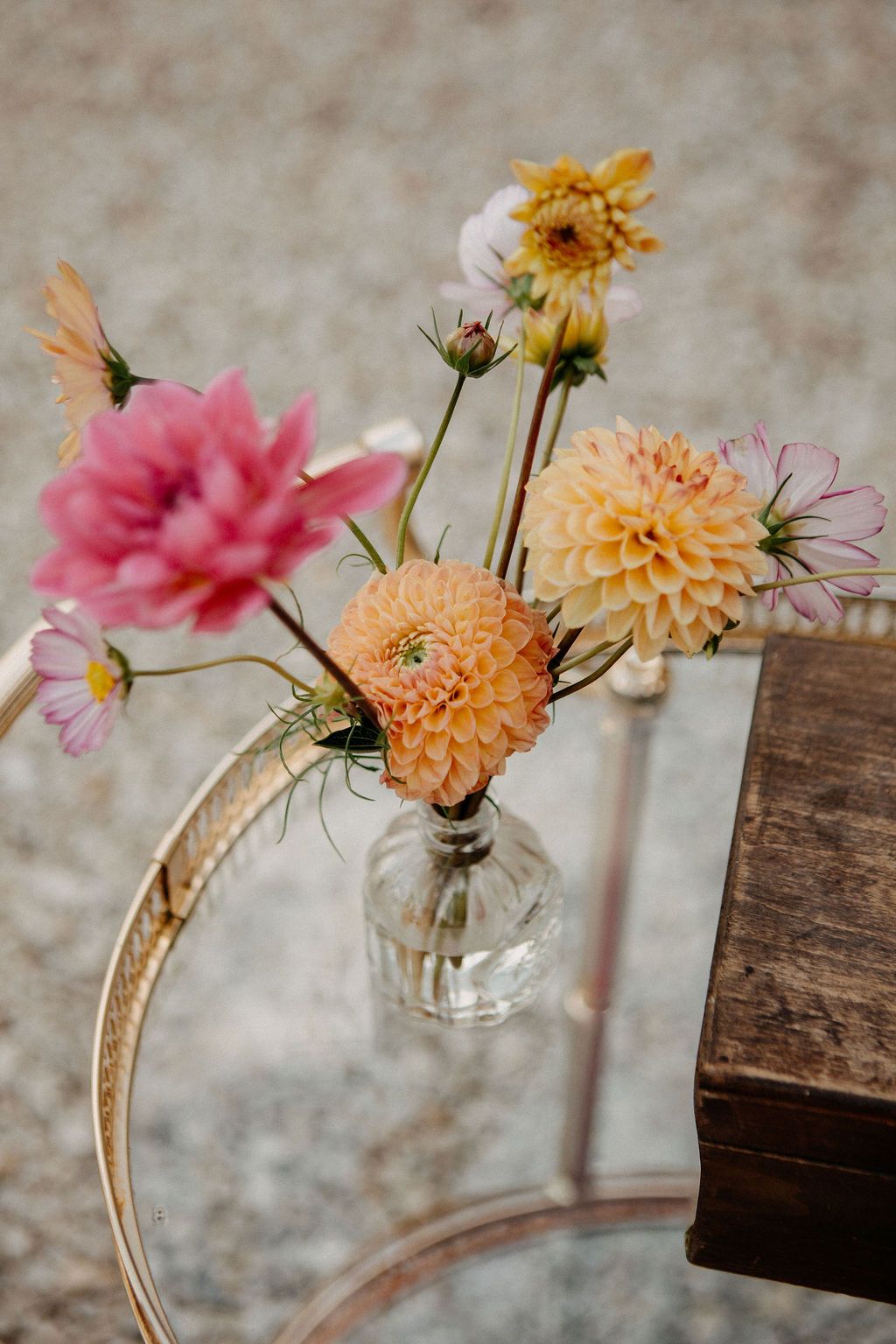 Colorful pink and peach dahlias in glass vase on vintage gold bar cart at wedding.