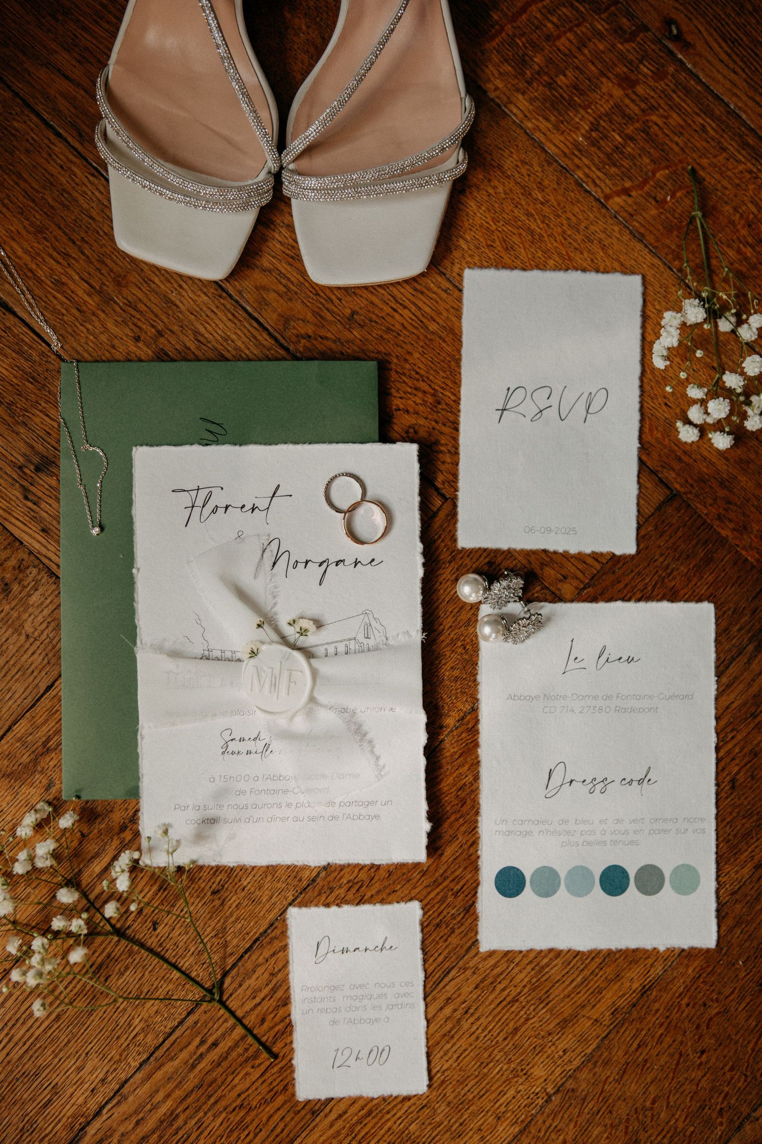Elegant wedding stationery flatlay with RSVP cards, invitation suite, rings, and bridal heels on rustic wood floor.