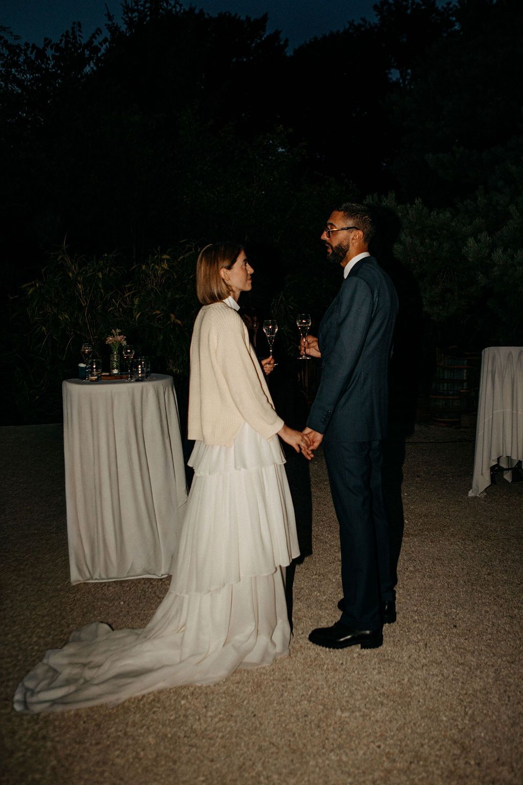 A bride and groom hold hands and share a romantic moment outdoors at their evening wedding reception.