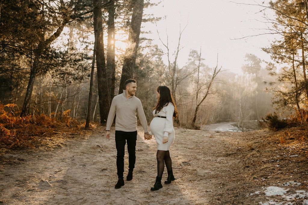 Couple holding hands walking on forest path bathed in golden autumn sunlight.