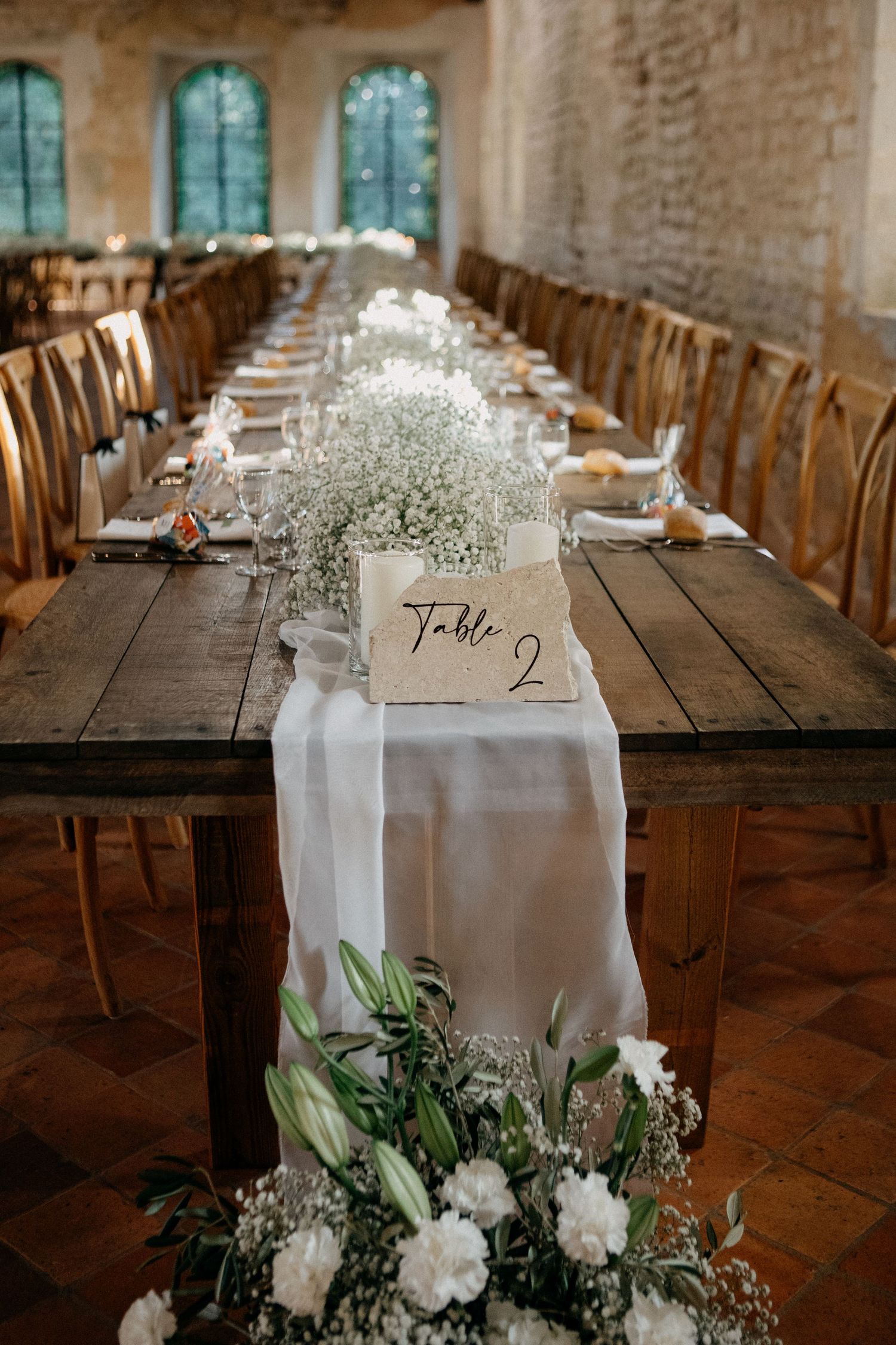 Long rustic wooden wedding table with white runner, baby's breath, and Table 2 sign.