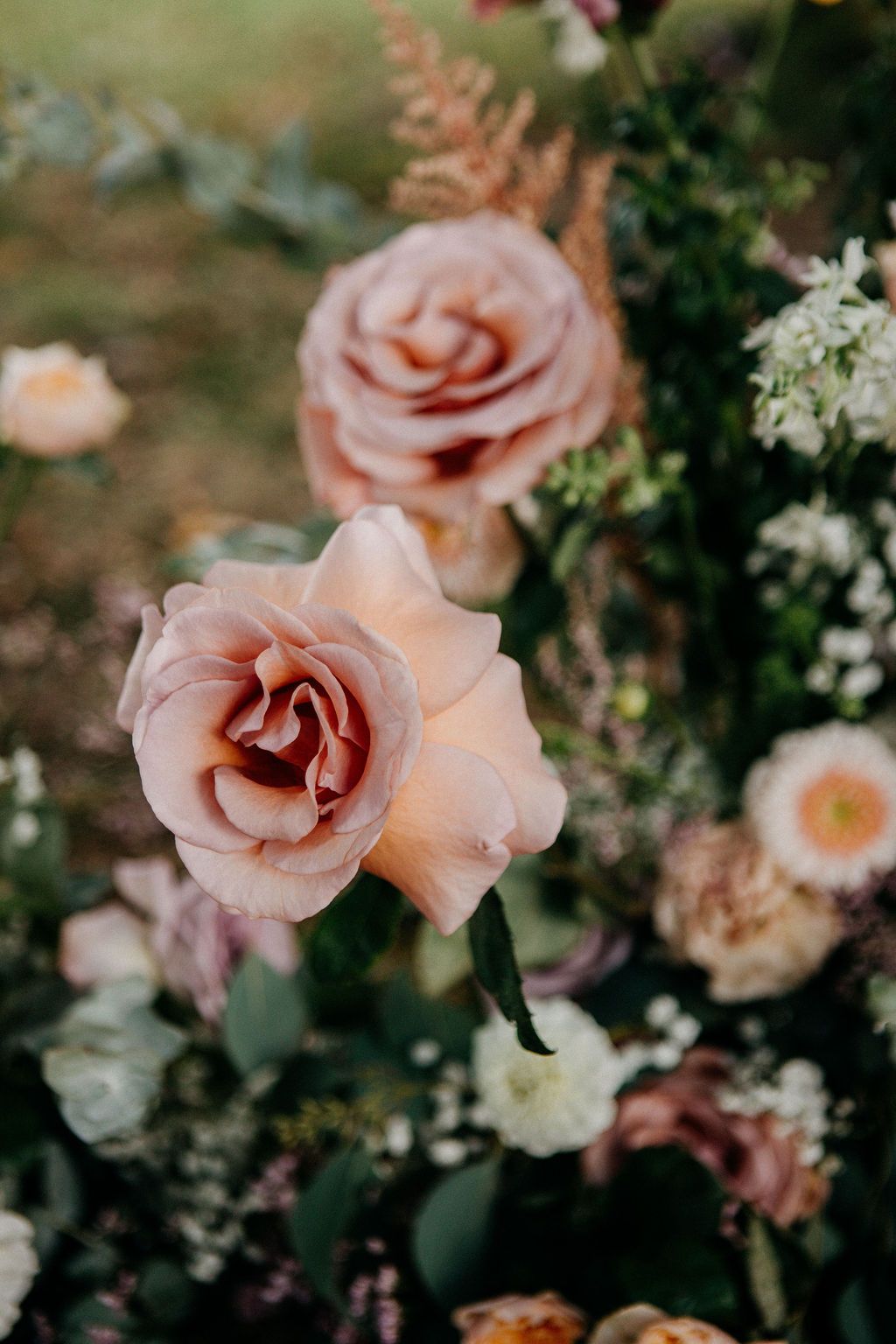 Close-up of blush pink roses and mixed florals in a romantic outdoor wedding flower arrangement.