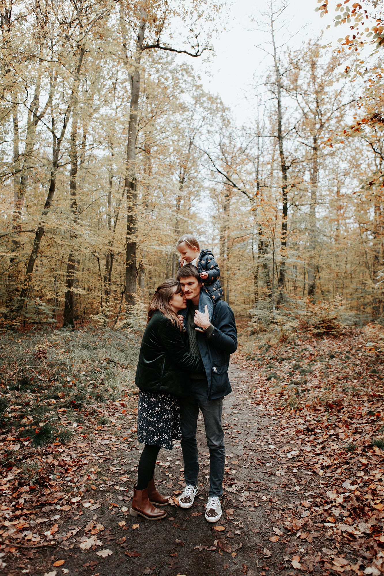 Family of three enjoying autumn forest walk, child sitting on fathers shoulders.
