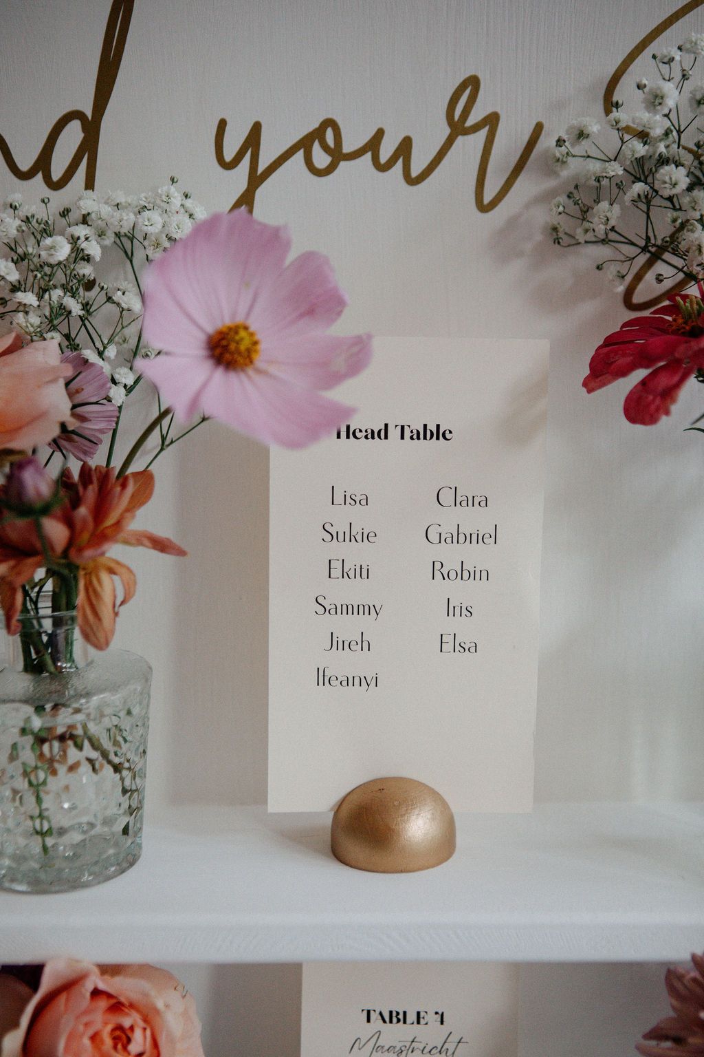 Wedding head table seating card displayed among pink cosmos and baby breath floral arrangements.