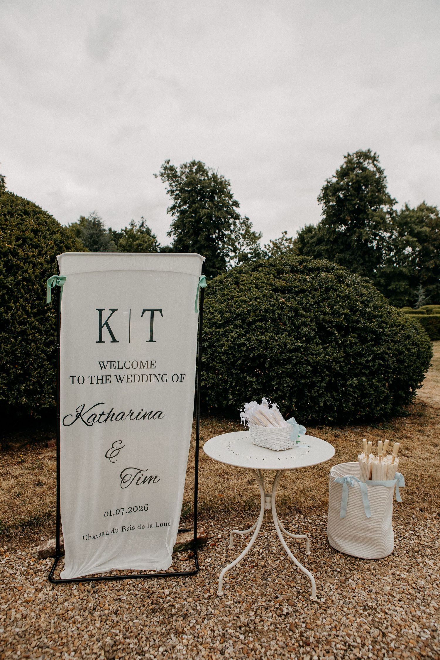Elegant outdoor wedding welcome sign for Katharina and Tim, dated 01.07.2025, displayed beside a white bistro table.