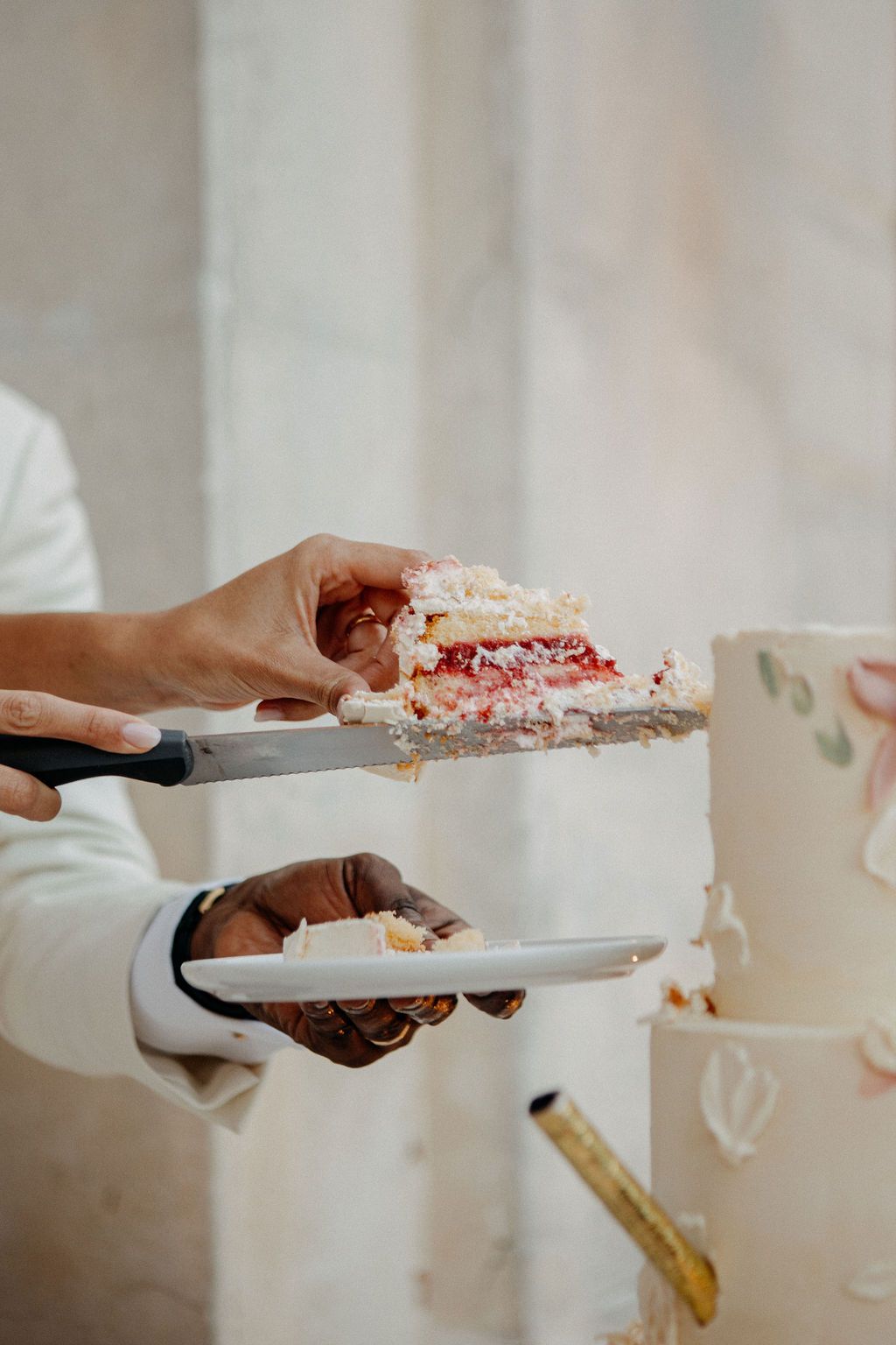 Close-up of hands serving a slice of layered strawberry wedding cake onto a white plate.