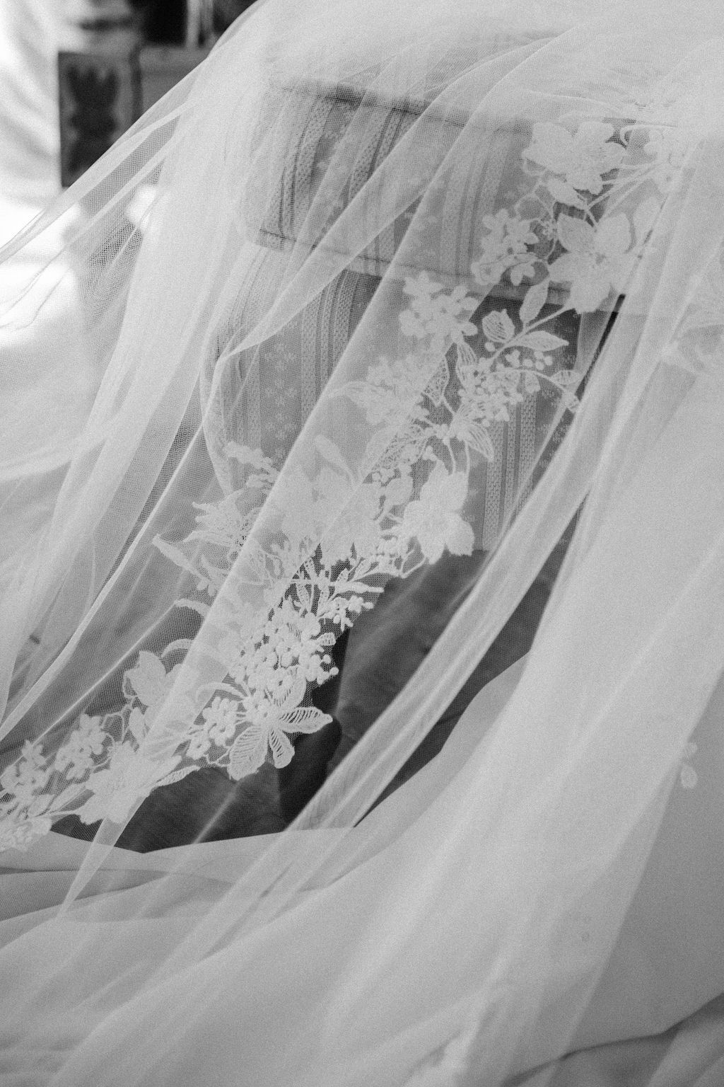 Close-up black and white detail of delicate floral lace trim on a bridal veil.