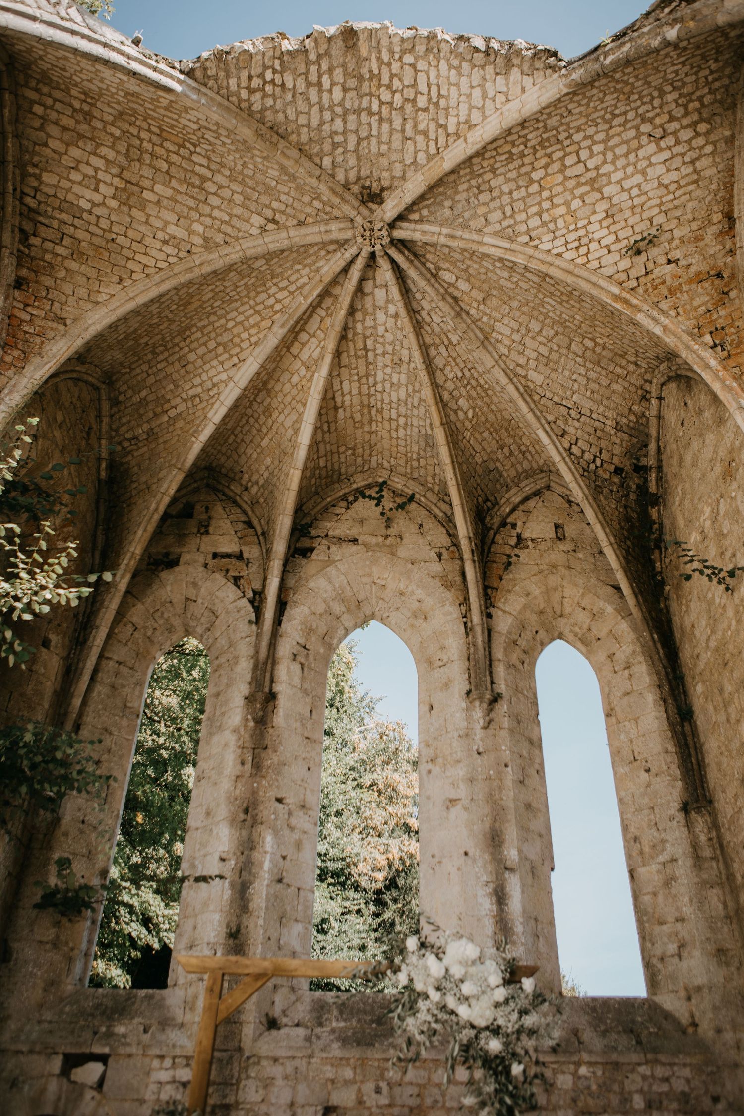 Gothic vaulted ceiling of a historic stone chapel ruins with arched windows open to blue sky above.