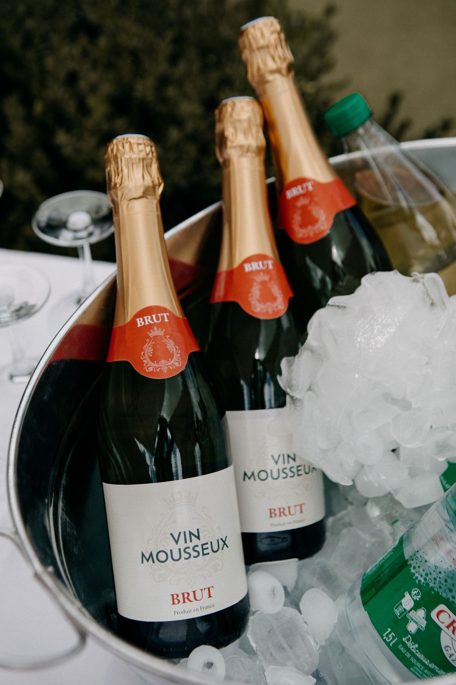 Three bottles of Vin Mousseux Brut champagne chilling in an ice bucket at an elegant outdoor event.