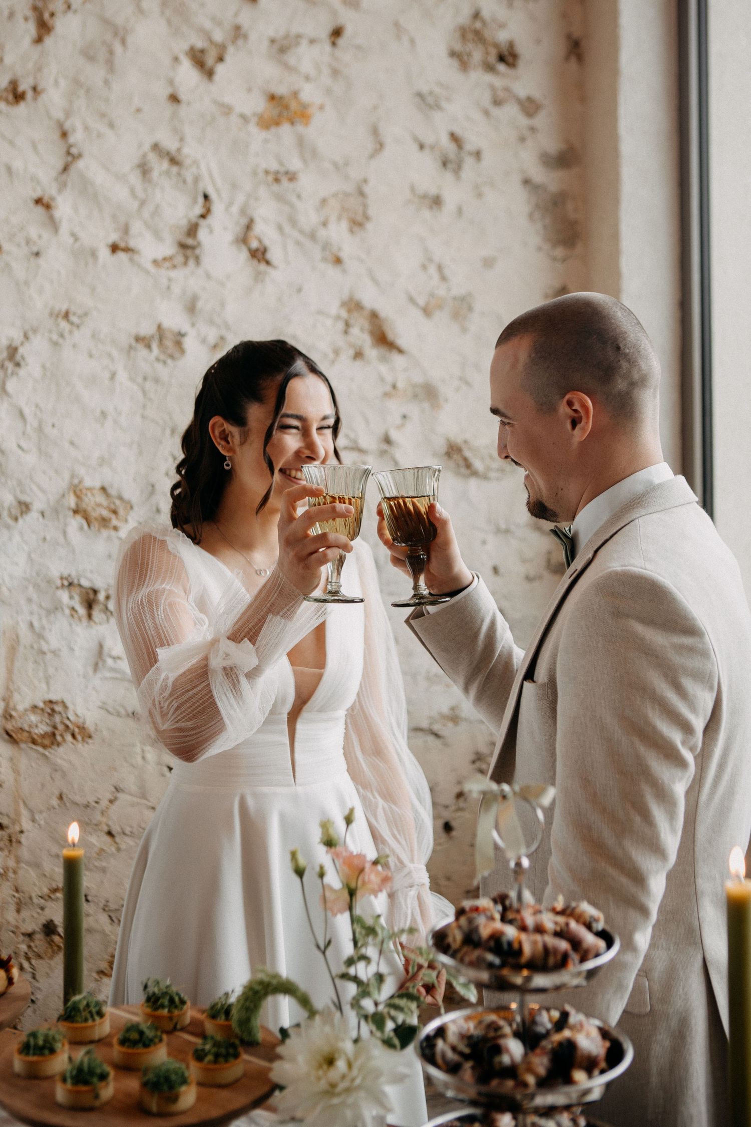Bride and groom toasting with elegant glasses at a rustic wedding reception table adorned with candles and floral arrangements.