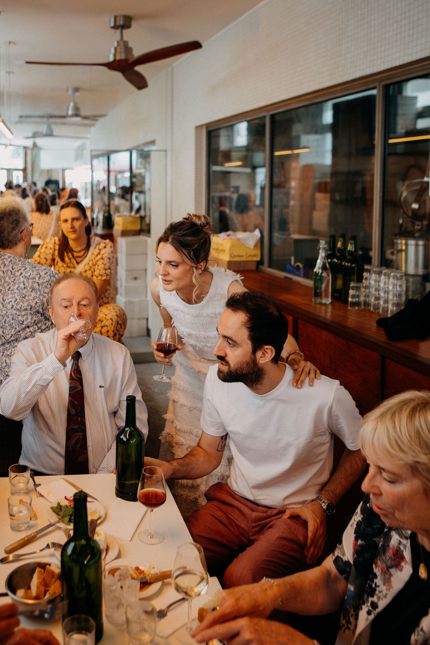 Guests dining at a restaurant, sharing wine and conversation around a table with bottles and plates.