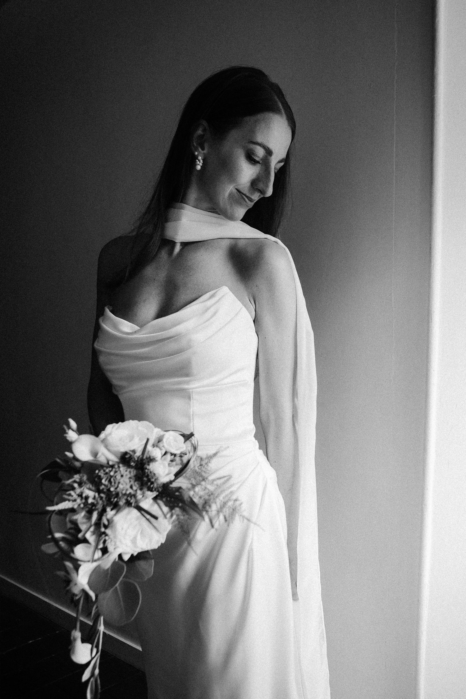 Black and white photo of a bride in a white gown holding a bouquet, smiling softly in elegant wedding attire.