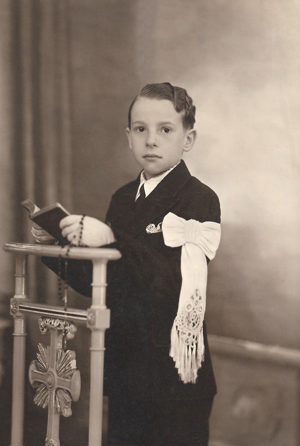 Vintage sepia portrait of a young boy dressed in dark suit holding a book at his First Communion.