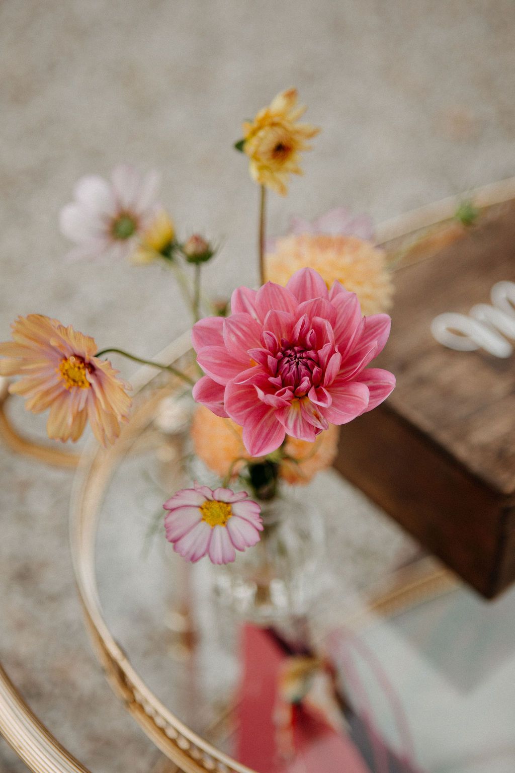 Pink dahlia and wildflowers in glass vase on gold mirrored tray at wedding reception.