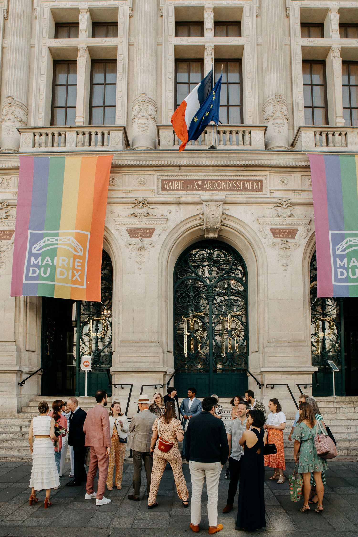 Guests gather outside Mairie du 10e arrondissement in Paris, decorated with rainbow Pride flags and the French tricolor.