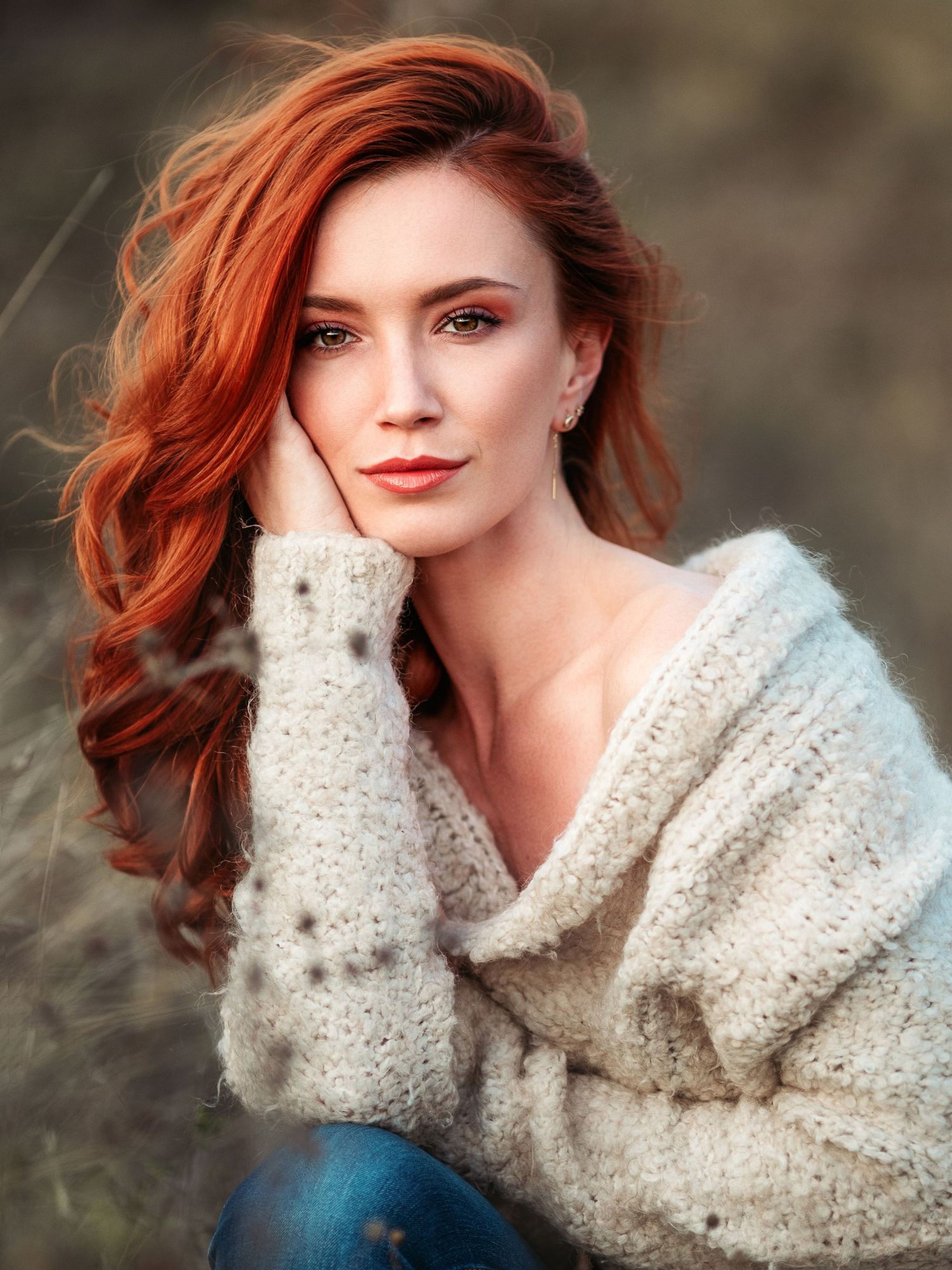 Portrait of woman in cozy sweater with vibrant red hair against natural background.