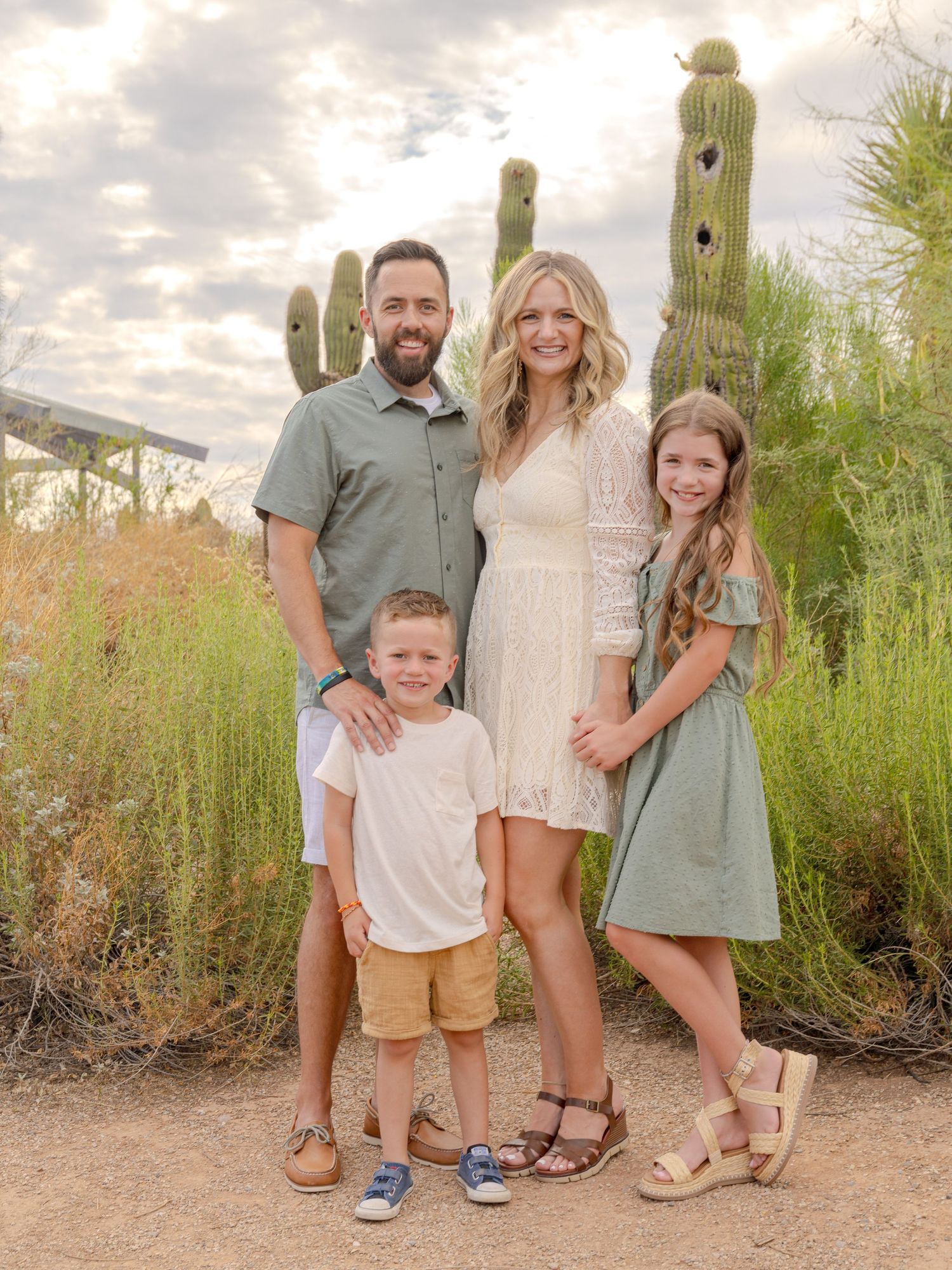 Family poses together in coordinated neutral outfits against desert landscape with cactus.