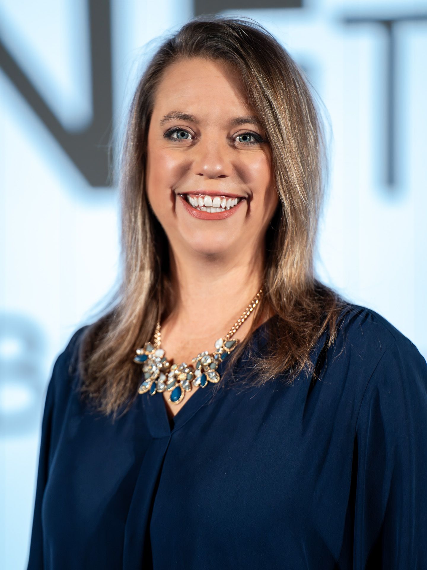 Professional portrait in navy dress with statement necklace against light background.
