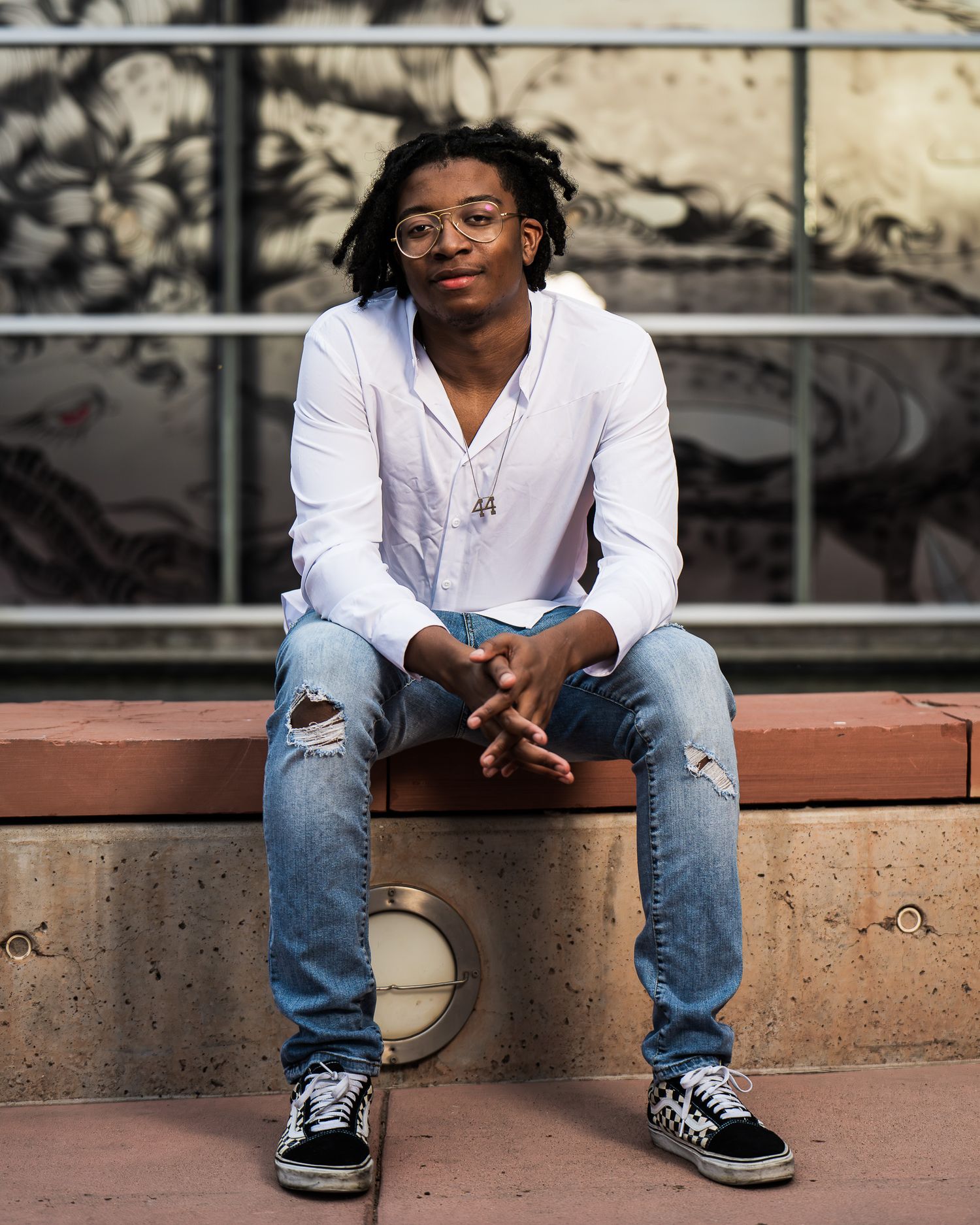 Casual portrait series of someone sitting on concrete steps wearing distressed jeans and sneakers.
