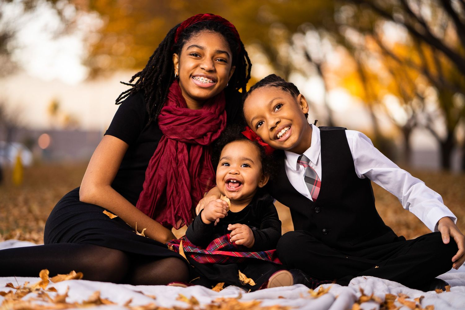 Family enjoying autumn day together on blanket with fallen leaves.