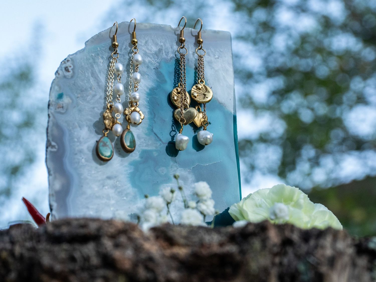 Collection of delicate gold and gemstone earrings displayed on blue glass.