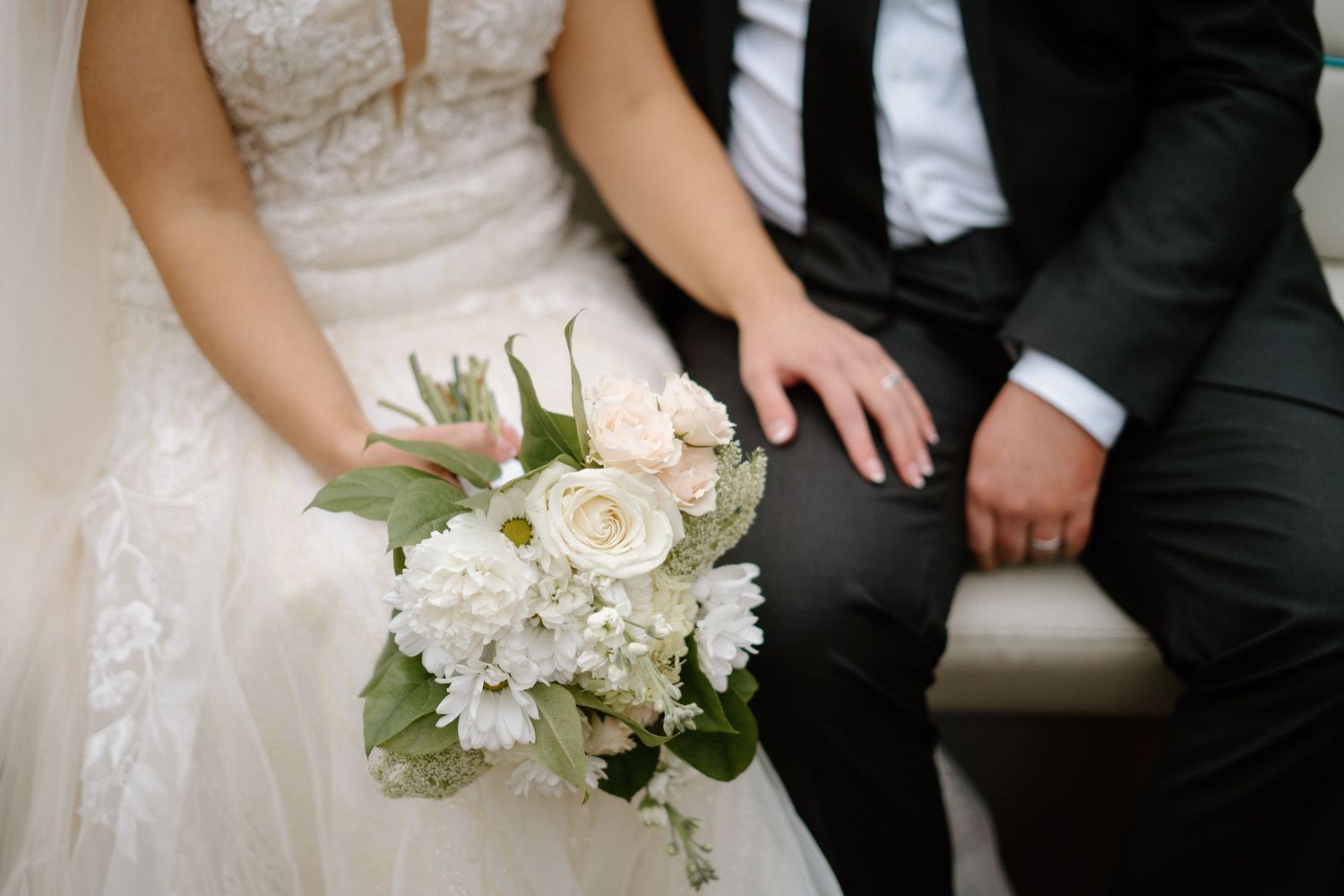 Wedding party members sit together on white steps while holding elegant white floral bouquets-Huntsville wedding photographer