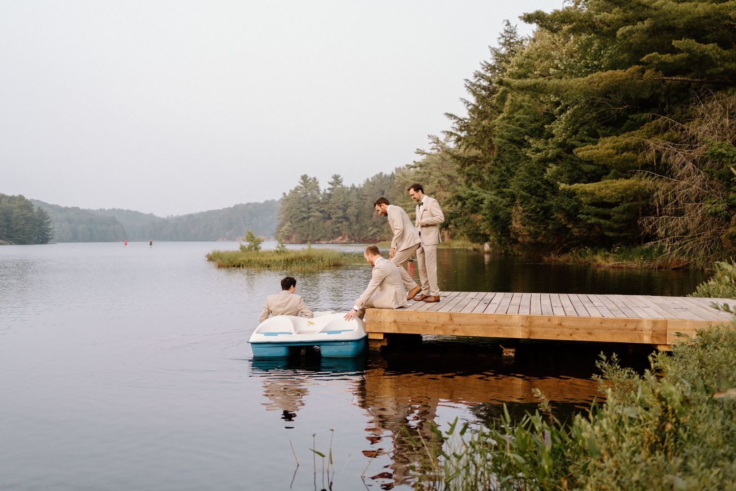 People enjoying a summer day relaxing on a wooden dock by a serene lake surrounded by pine trees.