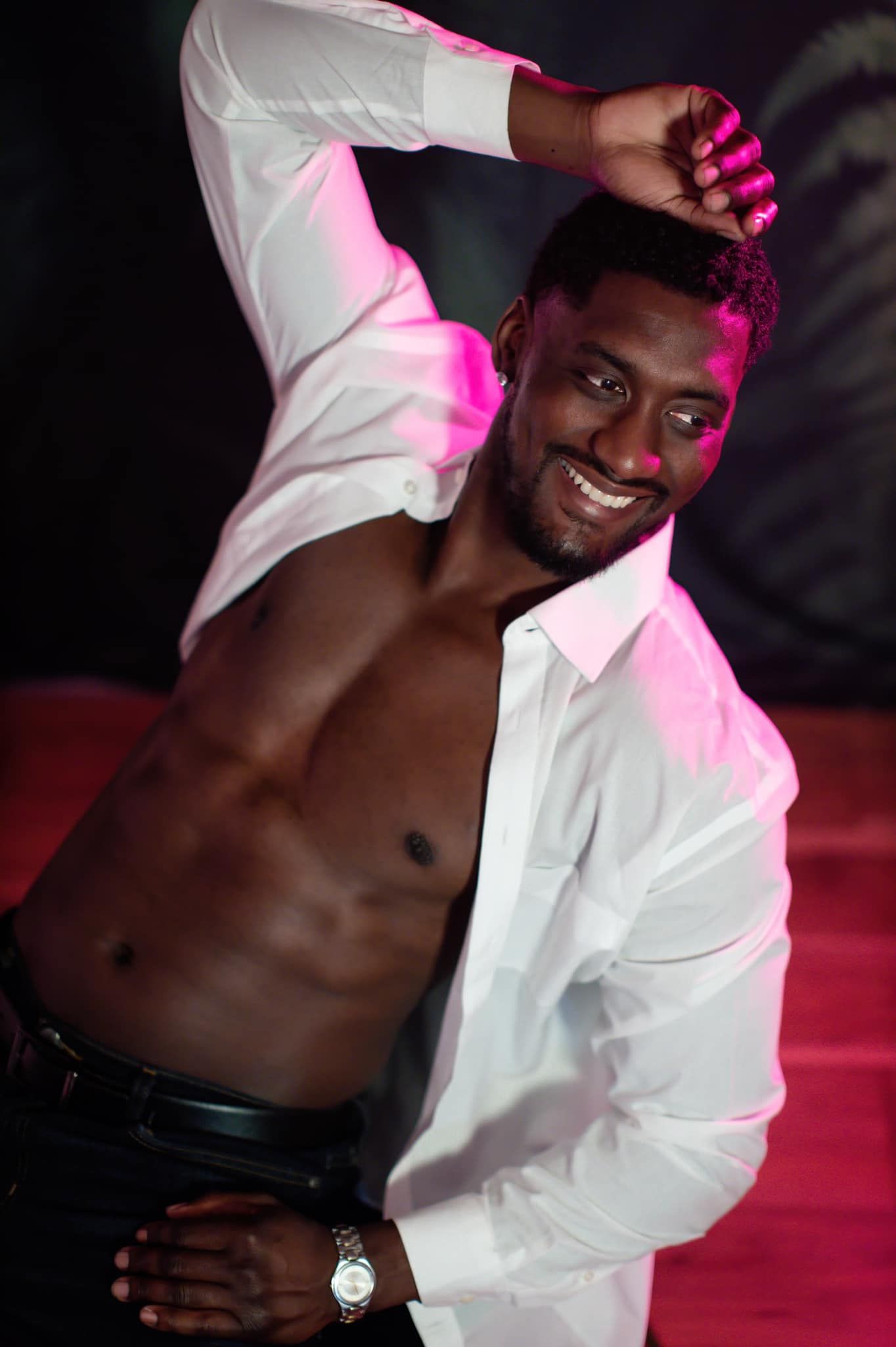 Portrait in white unbuttoned shirt under pink lighting.